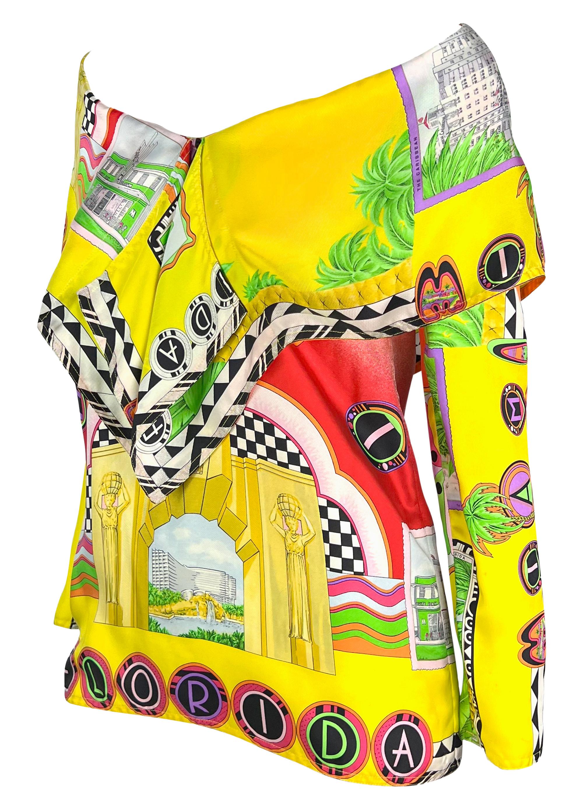 From the Spring/Summer 1993 Gianni Versace collection, this multi-color off-the-shoulder yellow 'Miami' print top highlights some of South Beach's most iconic Art Deco landmarks. This fabulous long-sleeved blouse features a v-neckline and fold-over