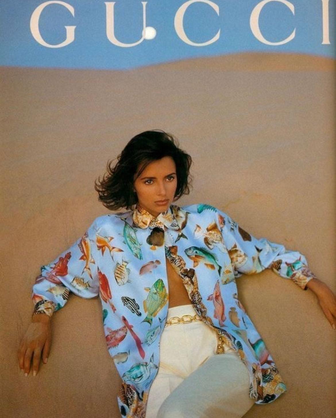 Présentation d'une chemise Gucci boutonnée en soie à motif aquatique bleu layette. Issu de la collection printemps/été 1992, ce fabuleux haut est apparu sur les podiums et dans la campagne publicitaire de la saison. Couverte de coquillages et
