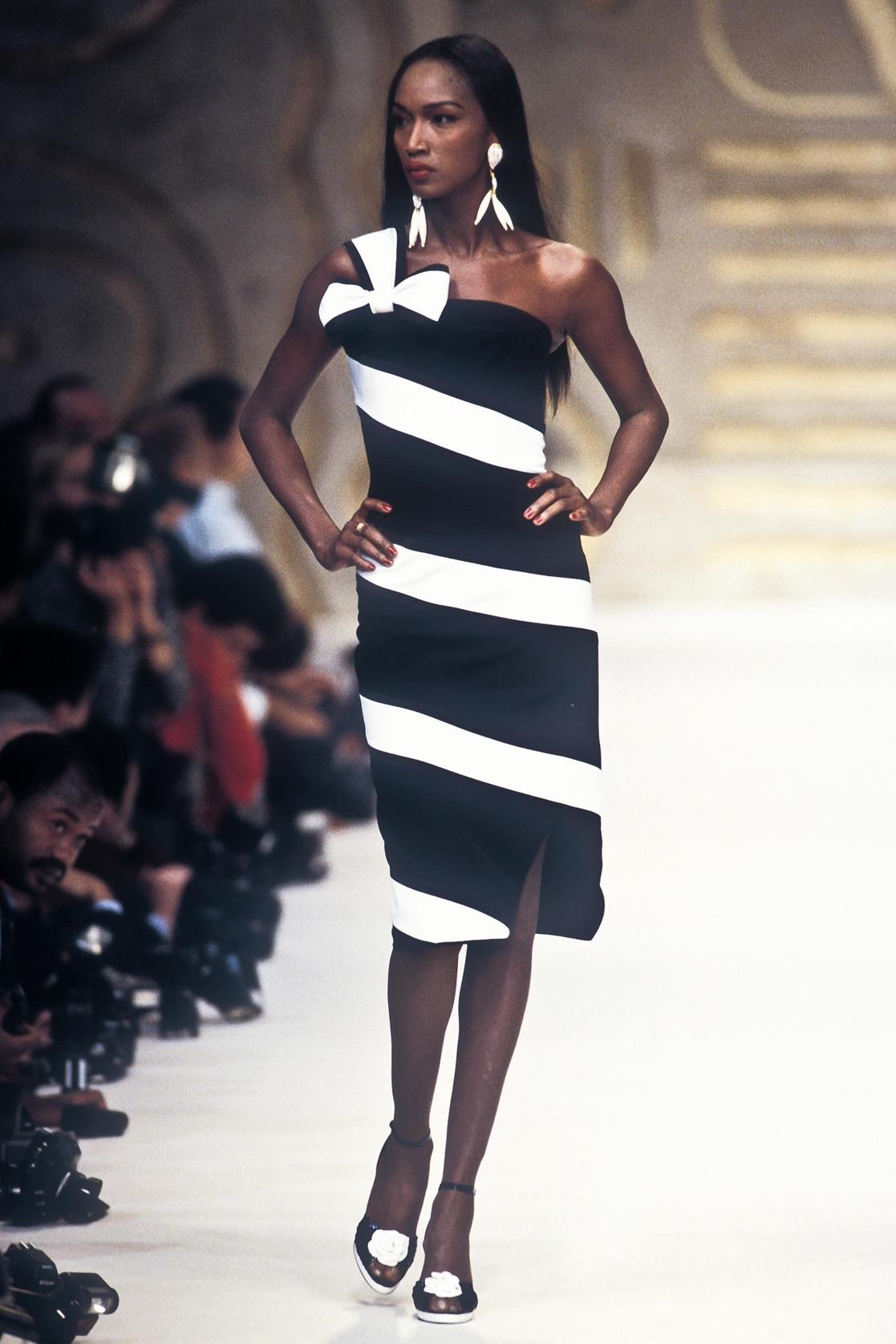 TheRealList presents: a black and white Valentino mini dress. From the Spring/Summer 1993 collection, this dress debuted on the season's runway on Katoucha Niane. The black silhouette is enlivened by a white ribbon, draped over one shoulder and tied