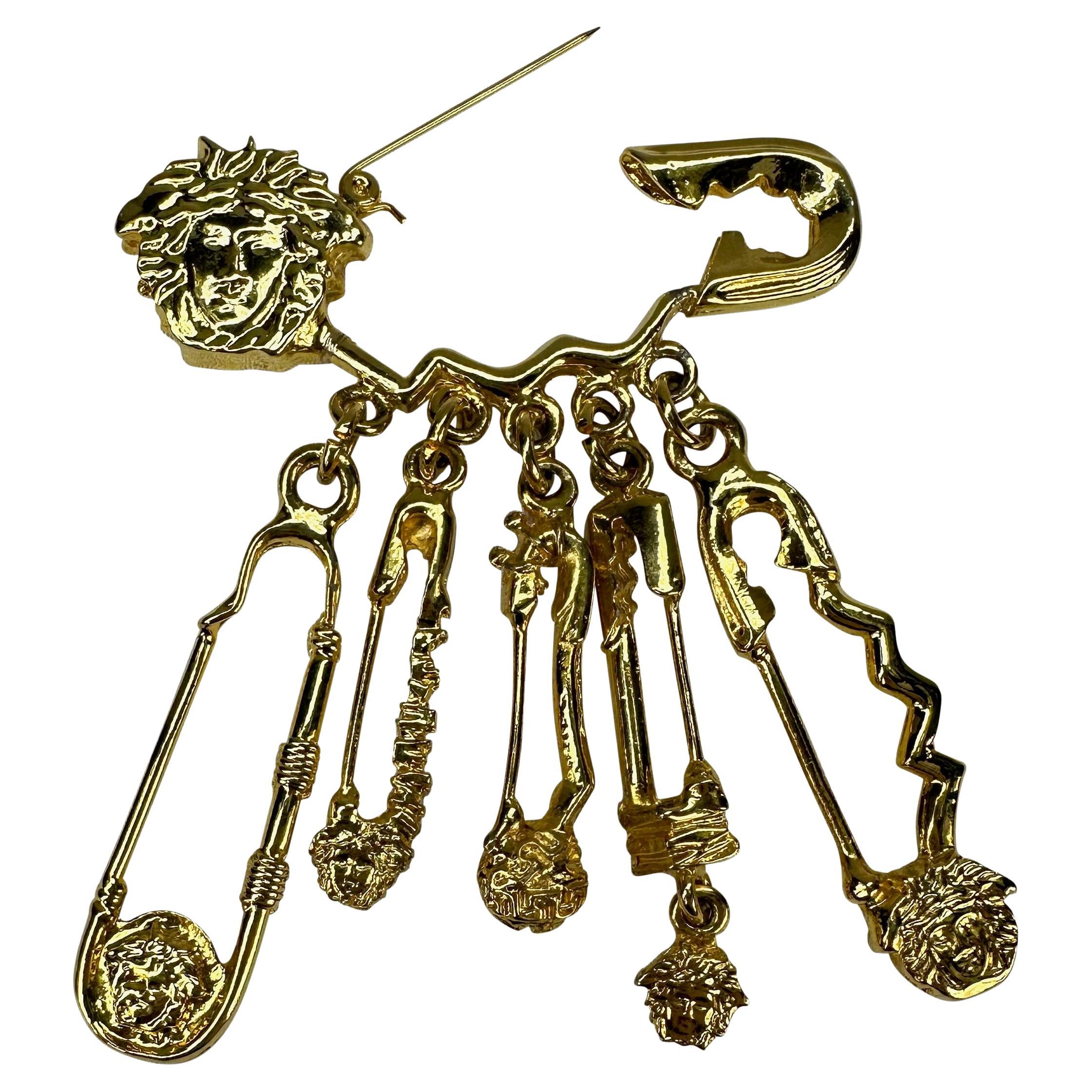 Voici une incroyable broche à épingle à nourrice Medusa de Gianni Versace en métal doré, conçue par Gianni Versace. Issue de la collection Printemps/Été 1994, cette broche à épingle à nourrice surdimensionnée est recouverte des logos de la Méduse de