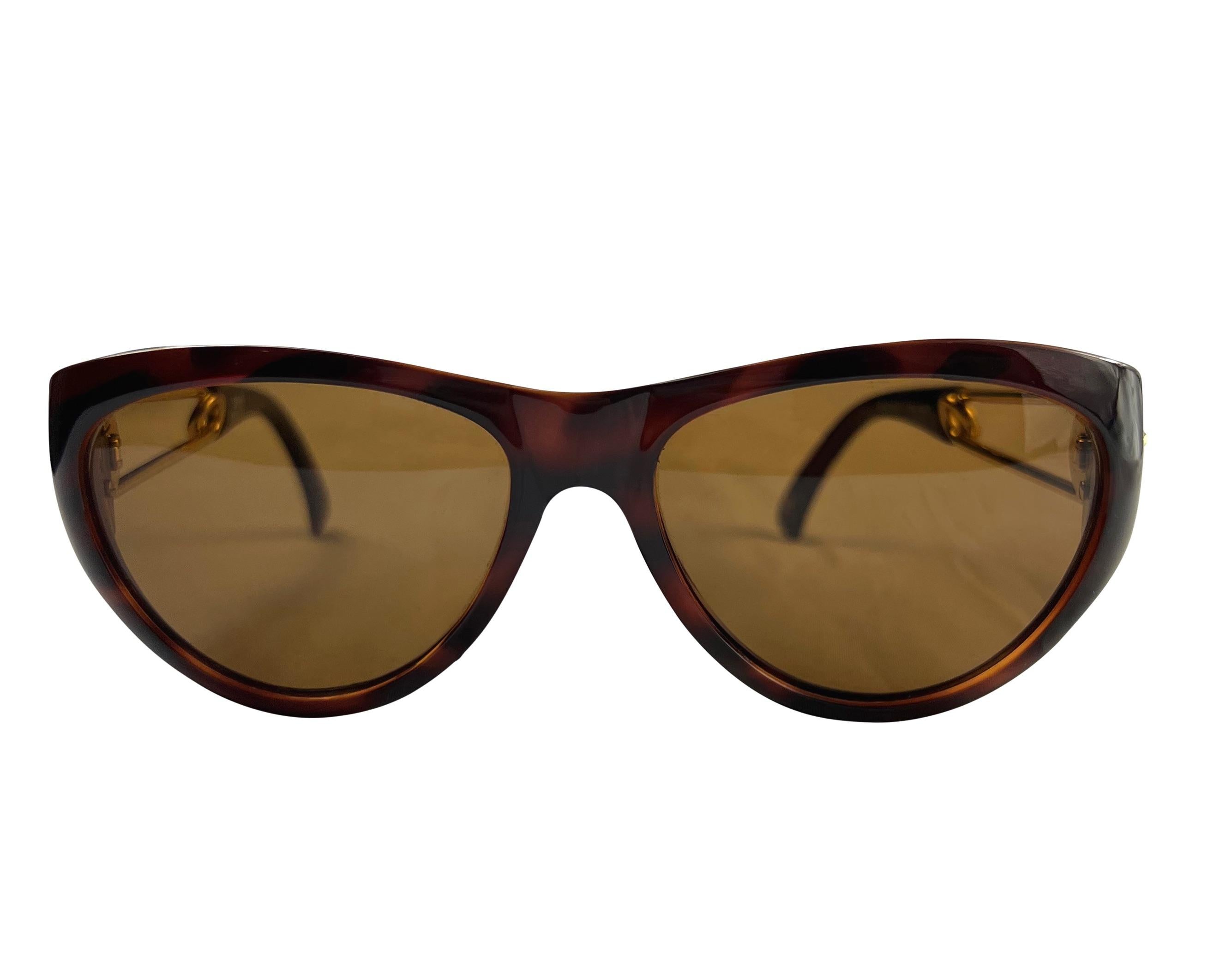 Wir präsentieren eine unglaubliche braune und goldfarbene Gianni Versace-Sonnenbrille, entworfen von Gianni Versace. Diese Sonnenbrille aus der Frühjahr/Sommer-Kollektion 1994 zeichnet sich durch ein subtiles Katzenaugen-Design und das berühmte
