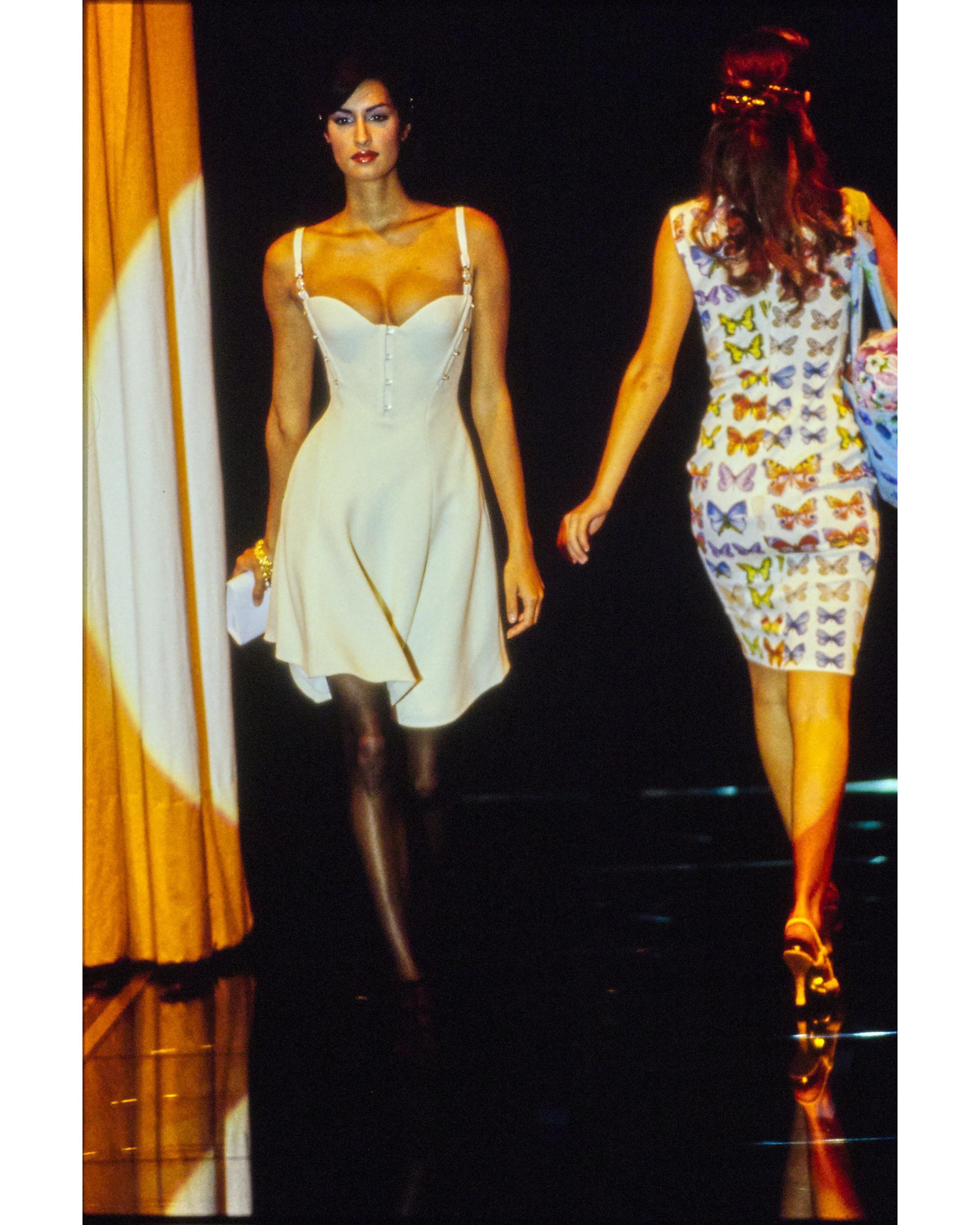 S/S 1995 Gianni Versace cream mini dress with signature Medusa head straps. Sleeveless dress with fitted bodice and flared A-line skirt, featuring bronze gold mini Medusa head closures at center front and sides. Built-in corset with boning and side