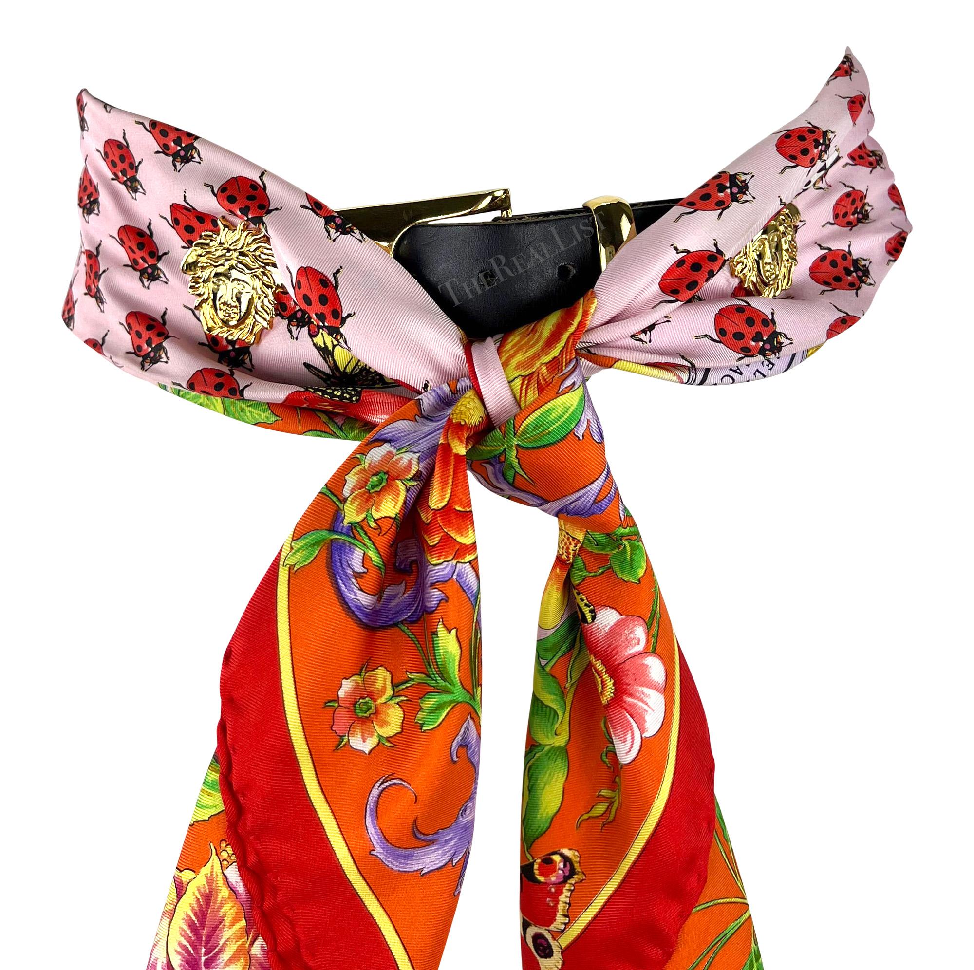 This pink scarf belt from Gianni Versace's Spring/Summer 1995 collection is crafted from silk and features a playful ladybug print. It includes large Versace Medusa medallions for decoration and a gold-tone buckle. The pink silk is covered with an