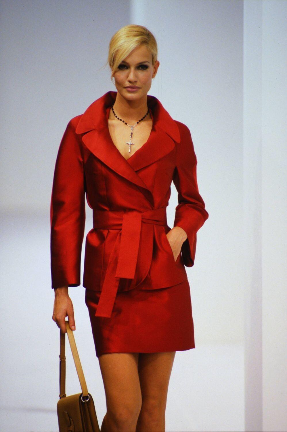 From Dolce & Gabbana’s Spring/Summer 1996 collection, this structured skirt suit is crafted from rich deep red silk satin taffeta. The jacket features dramatic wide lapels, a cinched waist with a matching self-tie belt, and a flared peplum hem.