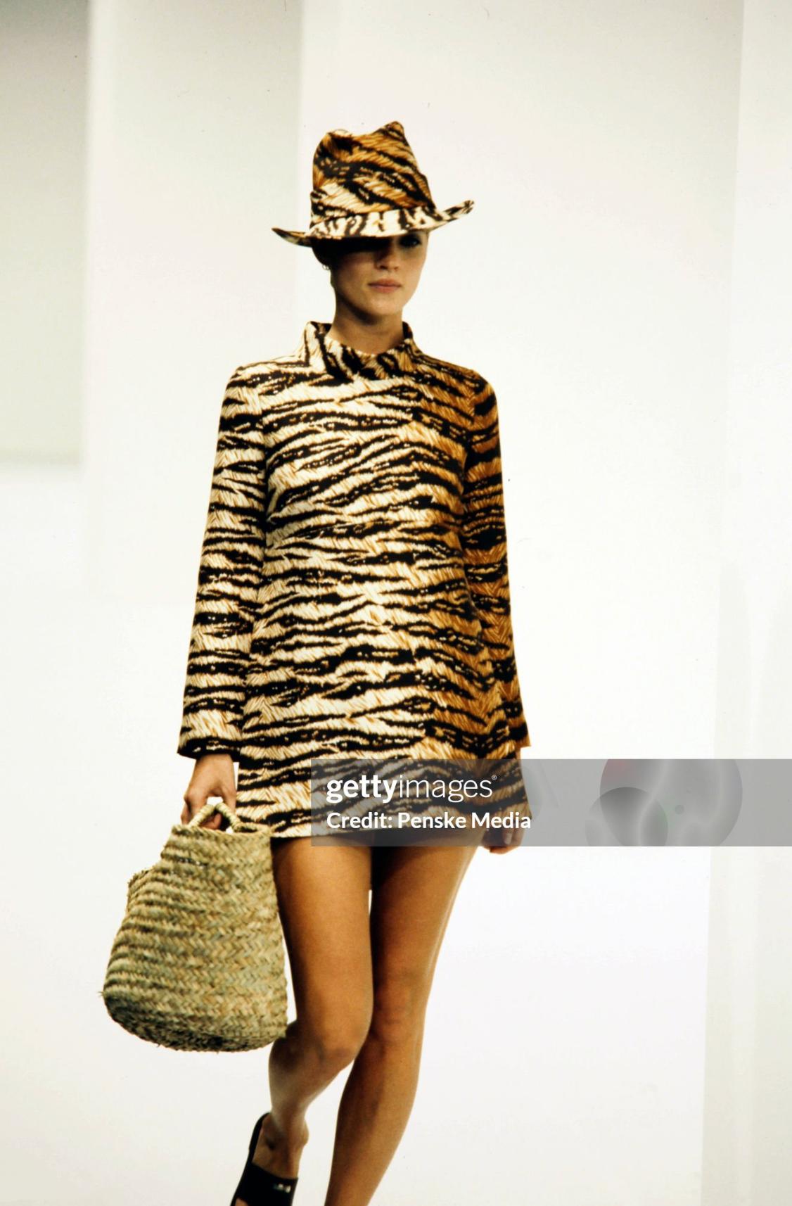 This Spring 1996 Dolce & Gabbana tunic top features a bold tiger print with a structured mock neckline and dramatic side slits. Worn by Kate Moss on the season's runway, this piece reflects the collection's inspiration—Monica Vitti's effortless