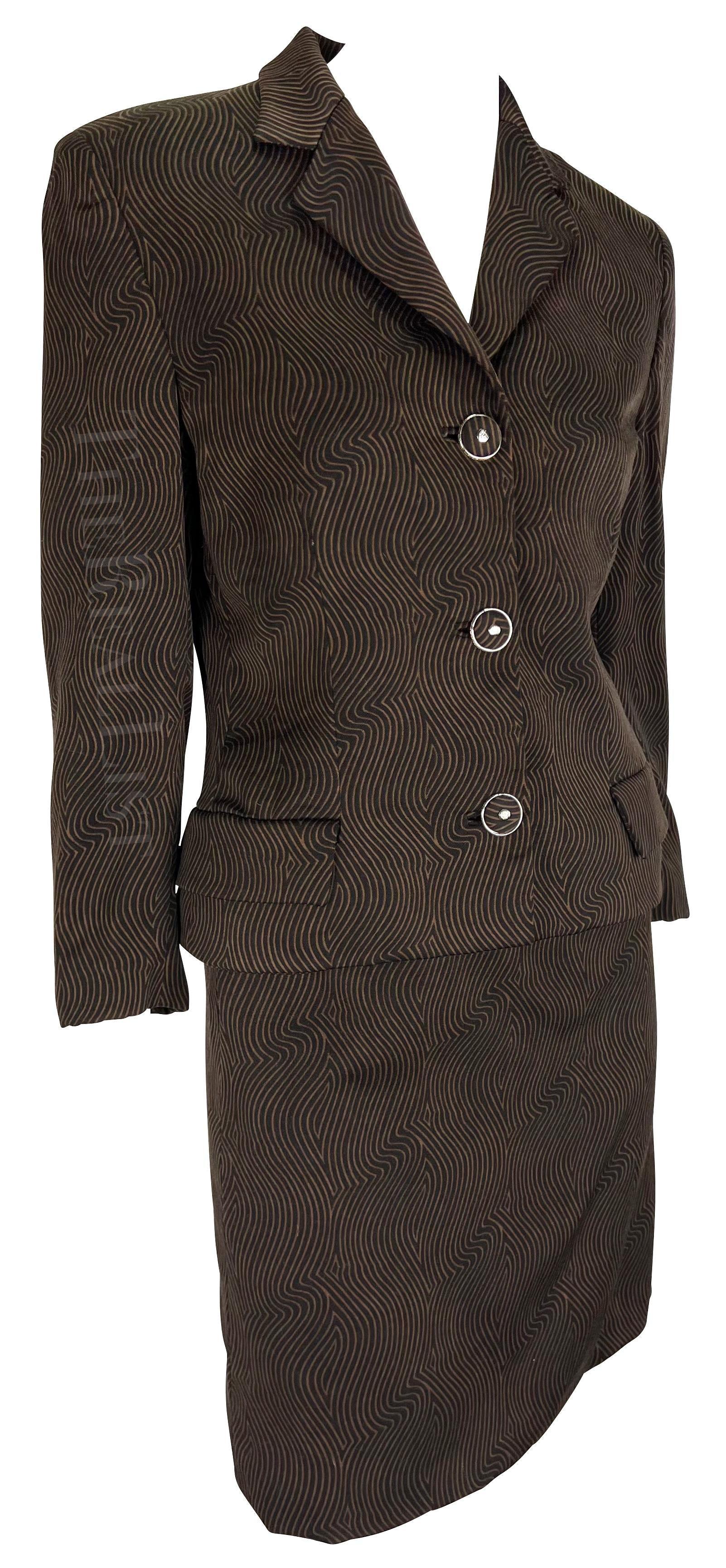 Voici un fabuleux tailleur jupe marron de Gianni Versace, dessiné par Gianni Versace. Issus de la collection automne/hiver 1996, la veste et la jupe assortie sont ornées d'un captivant imprimé linéaire ondulé. La veste, accentuée par un col Foldes