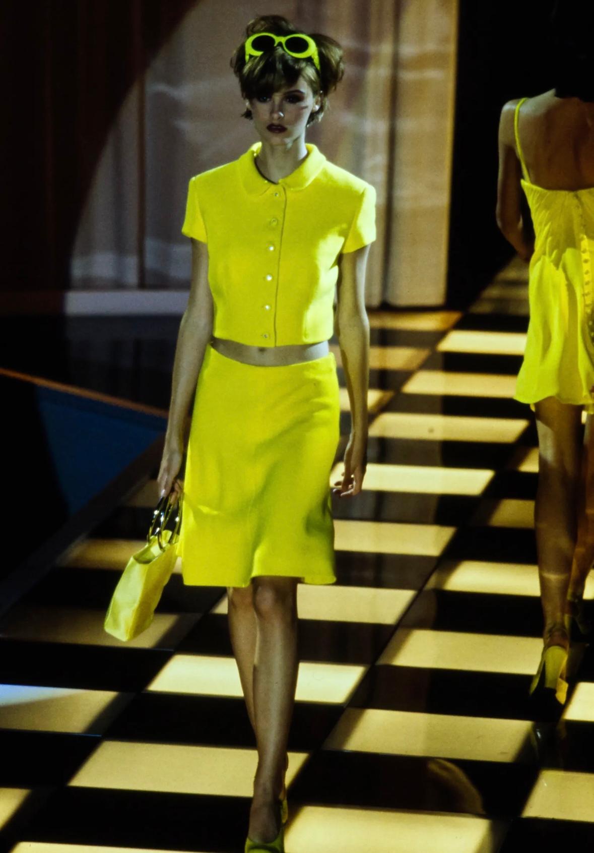 Dalla collezione Primavera/Estate 1996 di Gianni Versace, questo vibrante tailleur con gonna è realizzato in tessuto giallo neon stampato con un motivo floreale multicolore ispirato ai graffiti. Il set è composto da un blazer a maniche corte con