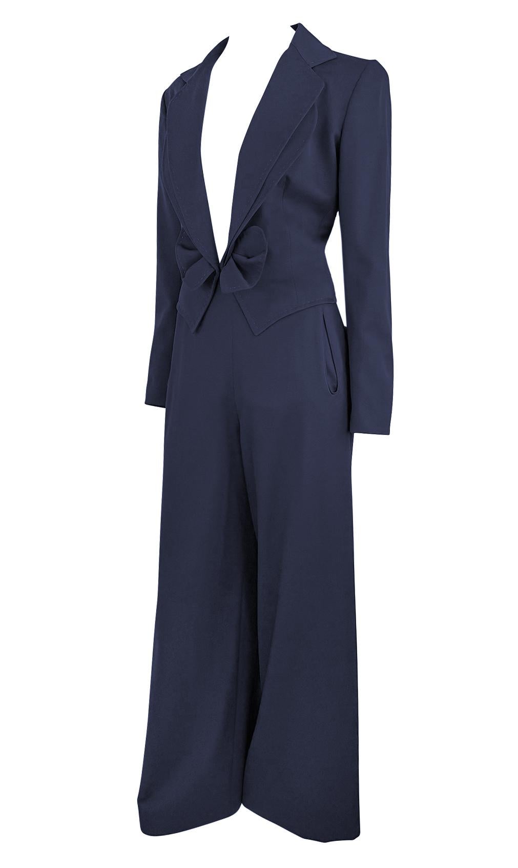 Ce tailleur pantalon bleu marine de la collection printemps/été 1997 de Givenchy, dessiné par John Galliano, présente une silhouette bien taillée avec un décolleté plongeant spectaculaire et des revers en pointe exagérés. La taille ajustée est