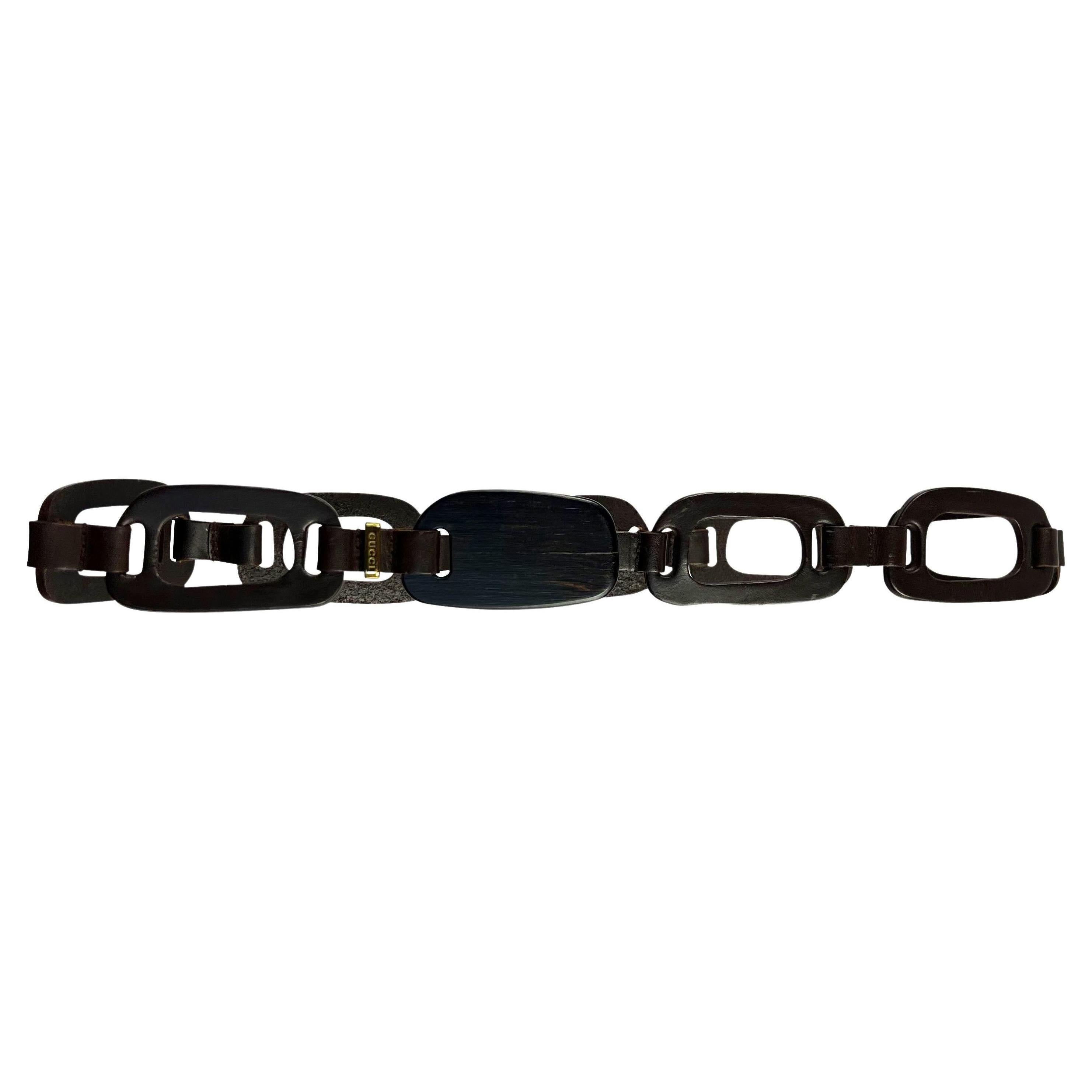 Voici une magnifique ceinture Gucci en cuir marron et bois, dessinée par Tom Ford. Issue de la collection printemps-été 1997, cette ceinture présente des anneaux découpés au laser reliés à des lanières de cuir et complétés par une boucle en bois.