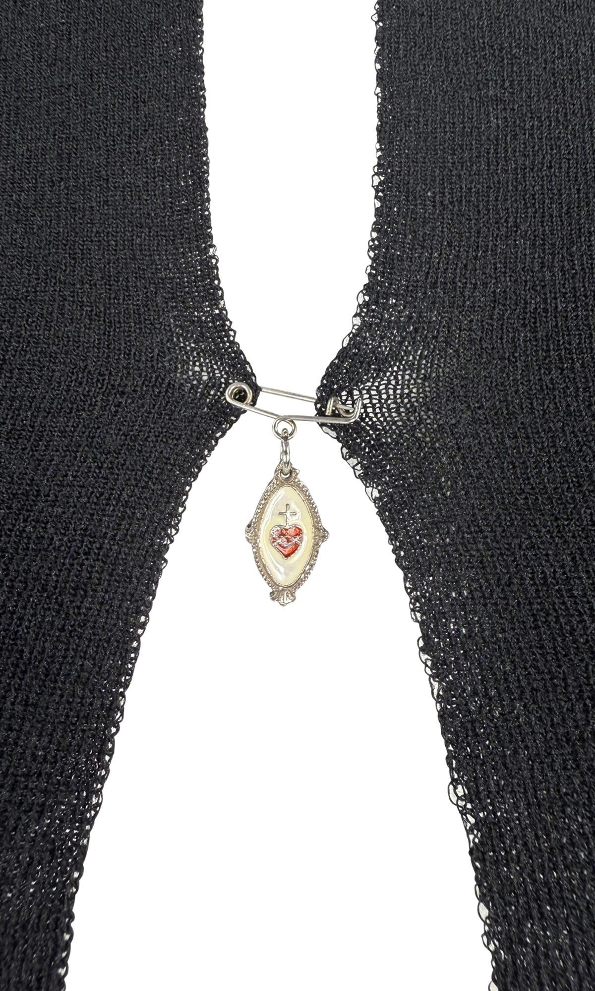 This Spring/Summer 1998 Dolce & Gabbana sleeveless top is crafted from black knit fabric with a striking open front. The bust is secured by a saftey pin closure bearing a signature sacred heart charm. 

Approximate measurements:
Size - removed
Bust: