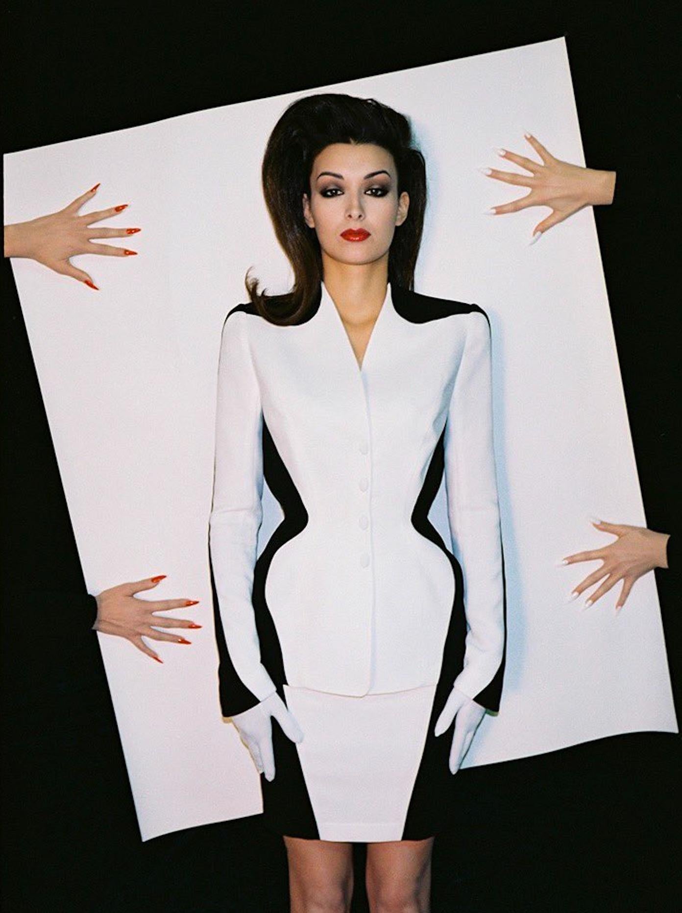 From Thierry Mugler’s Spring/Summer 1998 collection, this black and white color-blocked skirt suit features sharp tailoring and a sculpted silhouette. The jacket’s curved paneling accentuates the waist, while the structured shoulders and fitted