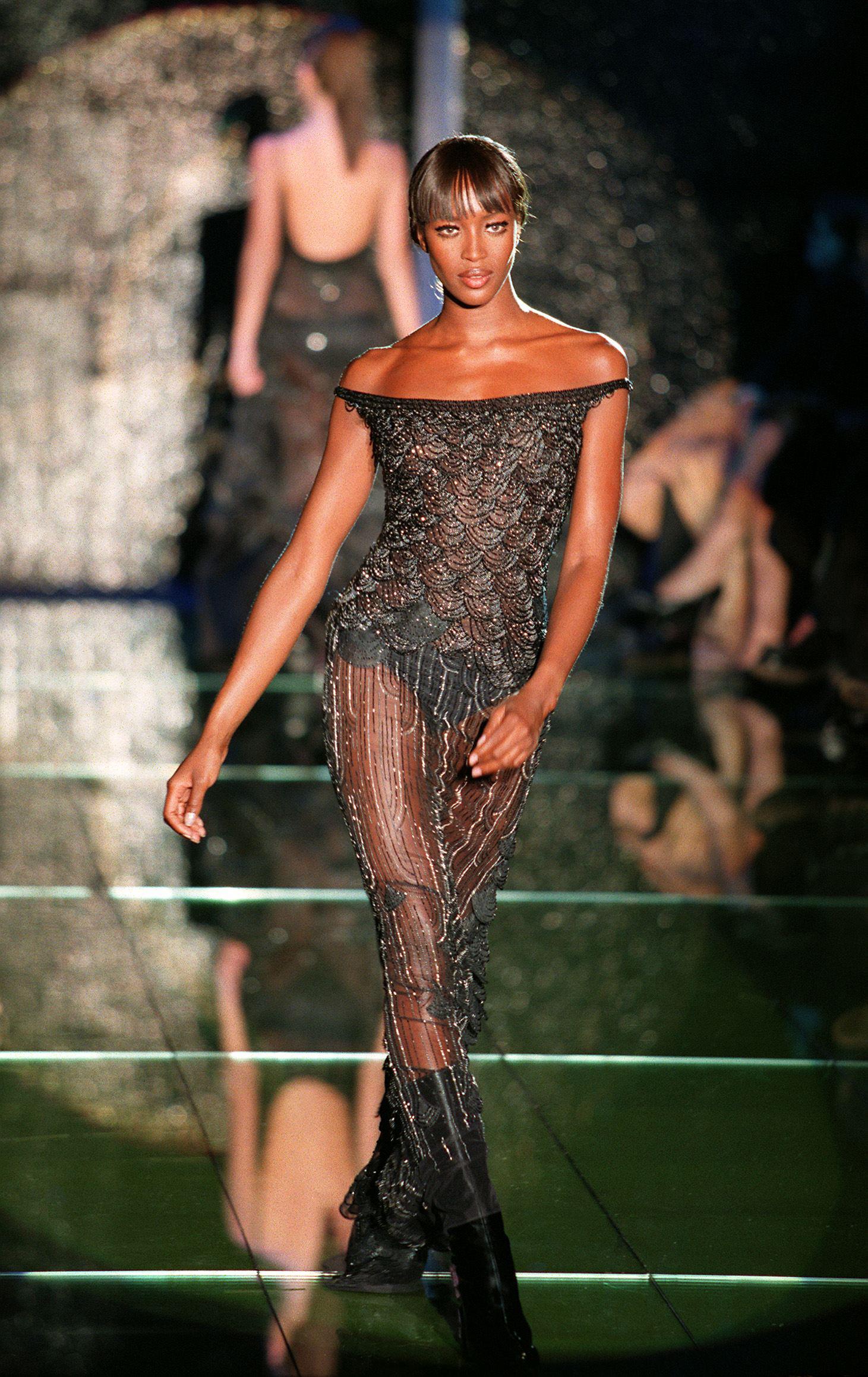 S/S 1999 Atelier Versace Haute Couture black mesh scallop embellished off-shoulder gown. Trained off-shoulder gown with fitted waist and heavily embellished 'scallop' upper with semi-sheer mesh contrasting lower, featuring long vertical and curved