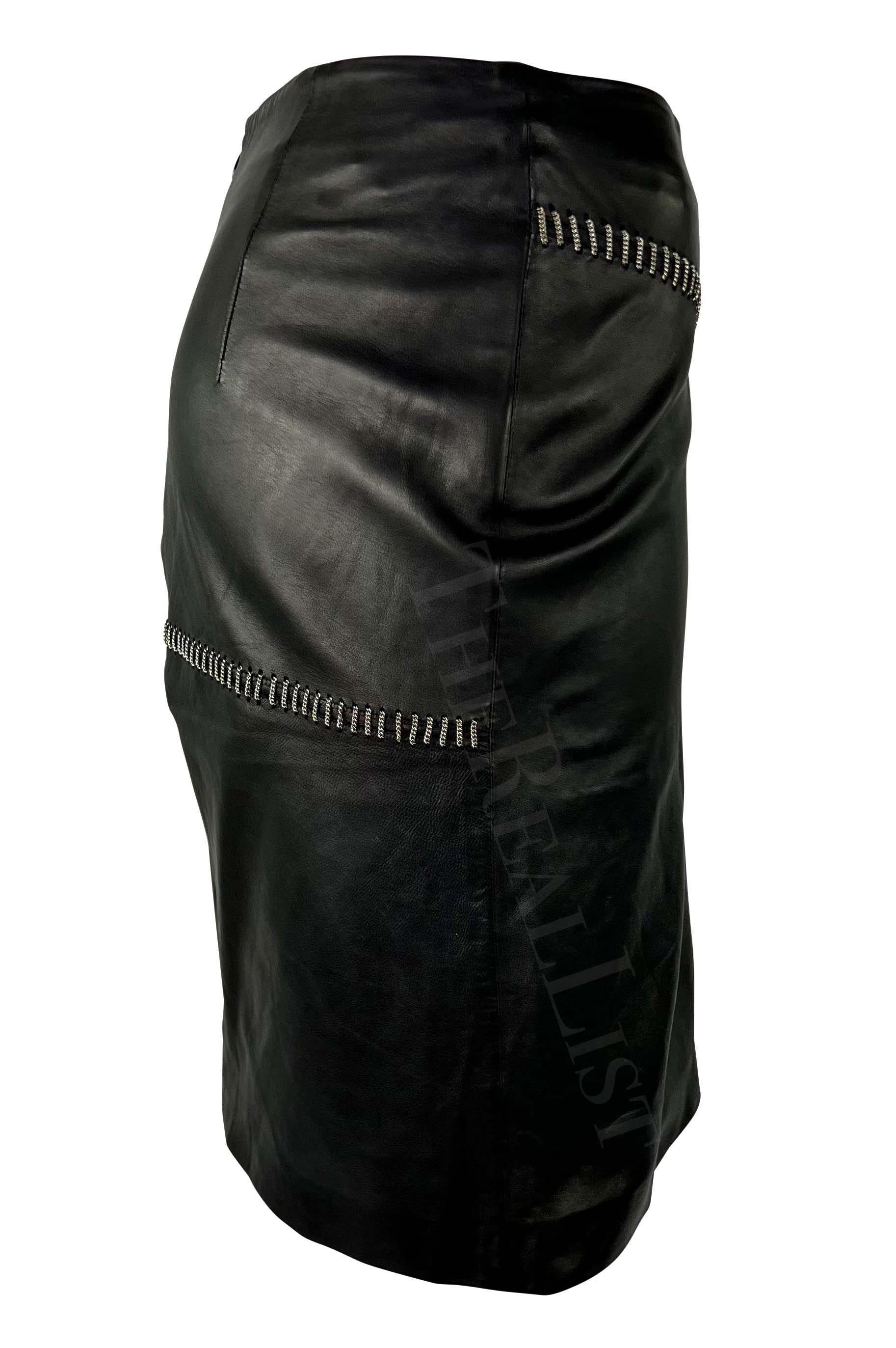 Ti presentiamo una favolosa gonna a tubino in pelle nera di Gianni Versace for Gianni Versace. Dalla collezione Primavera/Estate 1999, questa gonna è realizzata interamente in pelle ed è completata da un accento di catena asimmetrica intrecciata