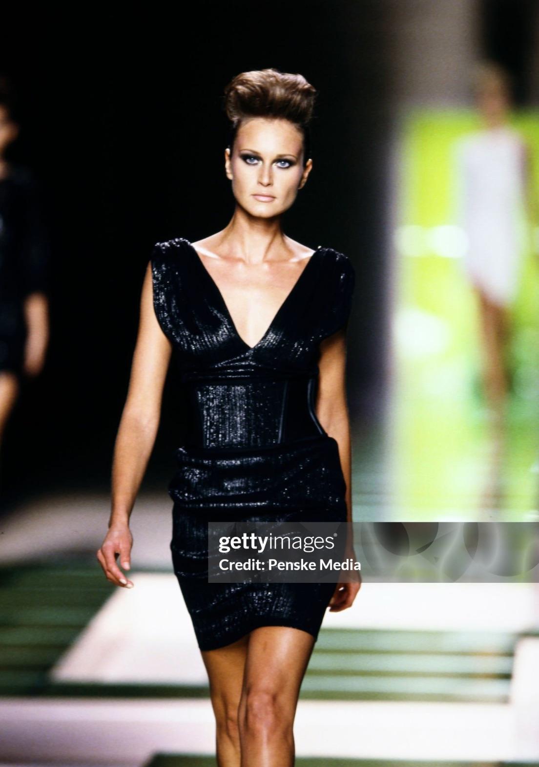 De la colección Primavera/Verano 2001 de Gianni Versace by Donatella, este minivestido blanco roto presenta un tejido brillante y una silueta elegante y ceñida al cuerpo. El escote pronunciado se acentúa con herrajes dorados de llave griega en los