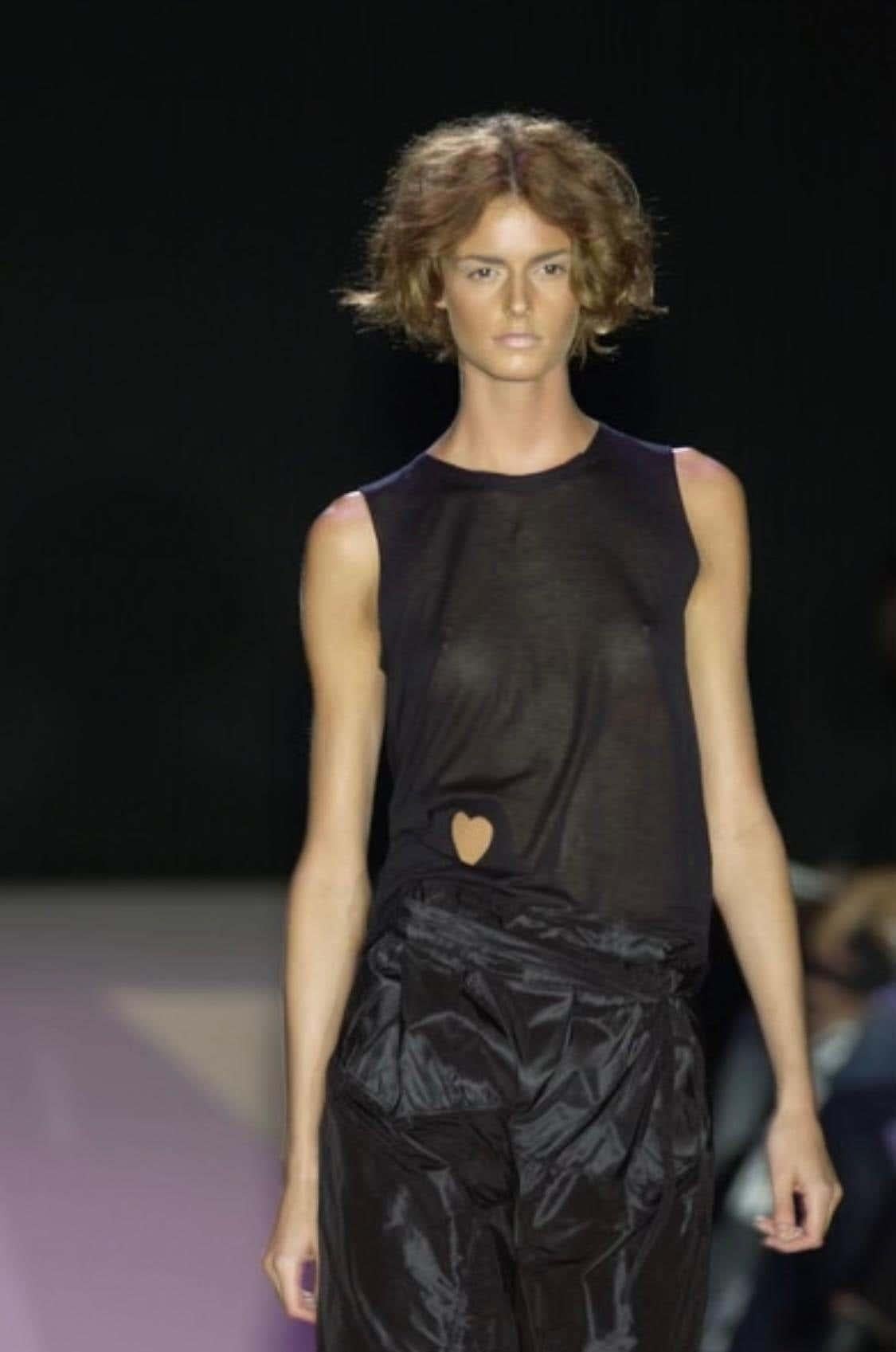 Ich präsentiere ein schwarzes, ärmelloses Gucci-Hemd, entworfen von Tom Ford. Dieses Oberteil aus der Frühjahr/Sommer-Kollektion 2002 wurde erstmals in Look 33 gezeigt, modelliert von Jacquetta Wheeler, während die weiße Version erstmals in Look 3