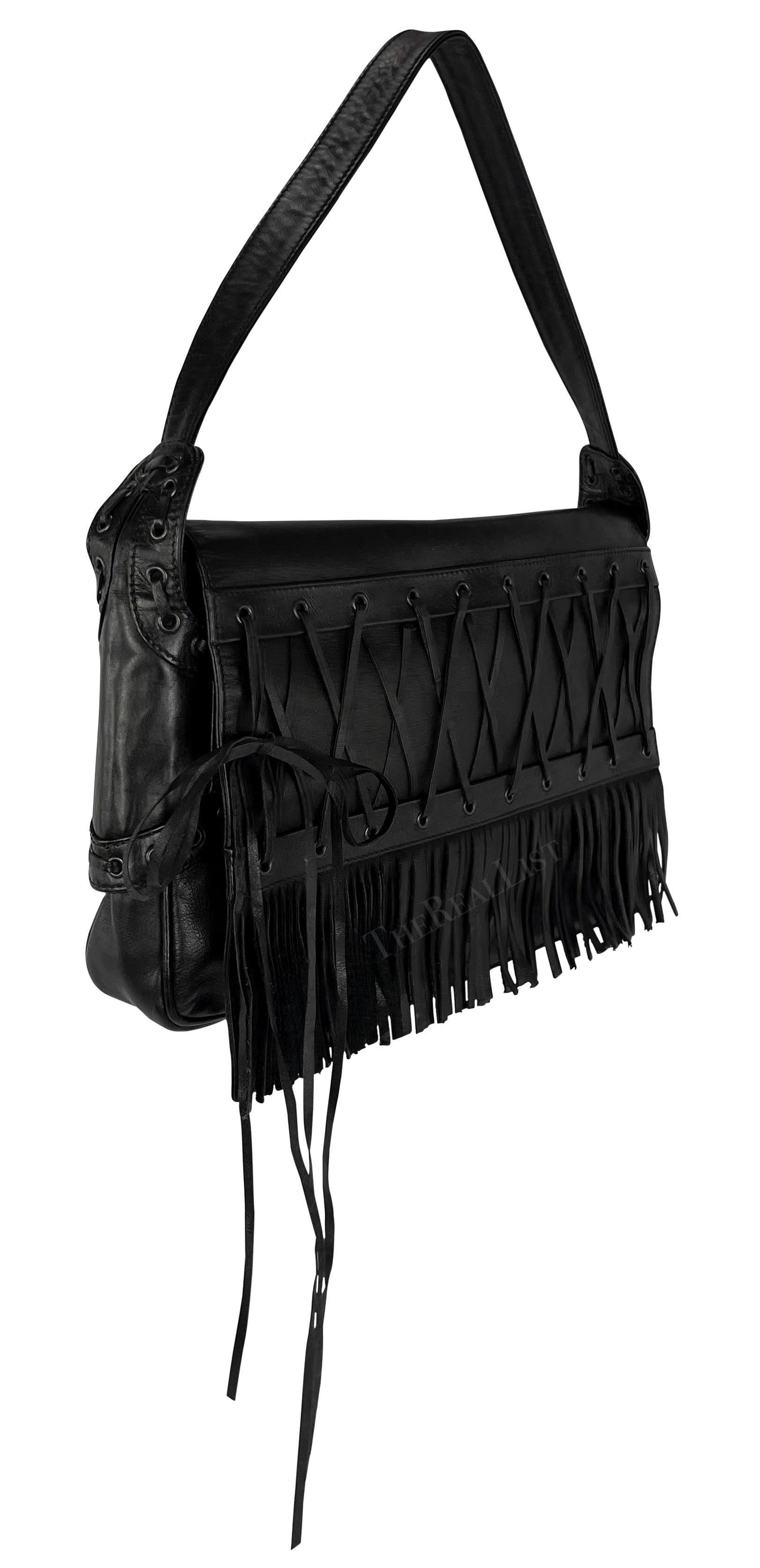 Ti presentiamo un'incredibile borsa a tracolla in pelle nera di Gianni Versace, disegnata da Donatella Versace per la collezione Primavera/Estate 2002. Questa borsa, realizzata interamente in pelle nera, presenta un accento di pizzo e frange sulla