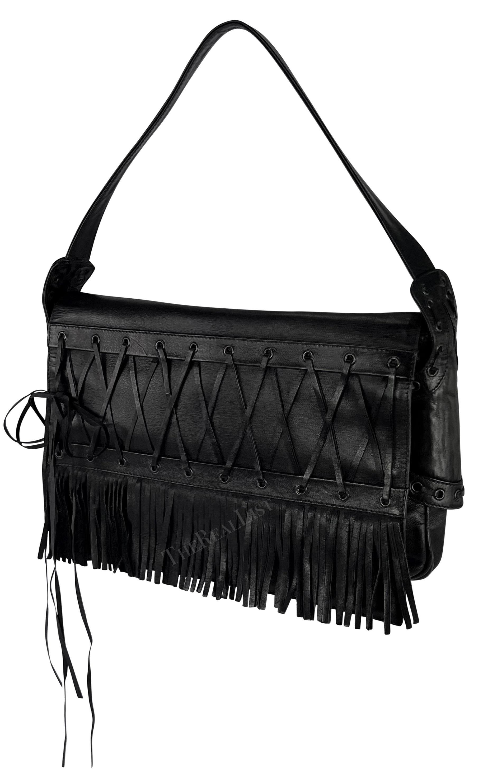 Presenting an incredible black leather shoulder bag by Gianni Versace, designed by Donatella Versace from the Spring/Summer 2002 collection. This bag, crafted entirely from black leather, showcases a lace-up accent and fringe on the front flap,