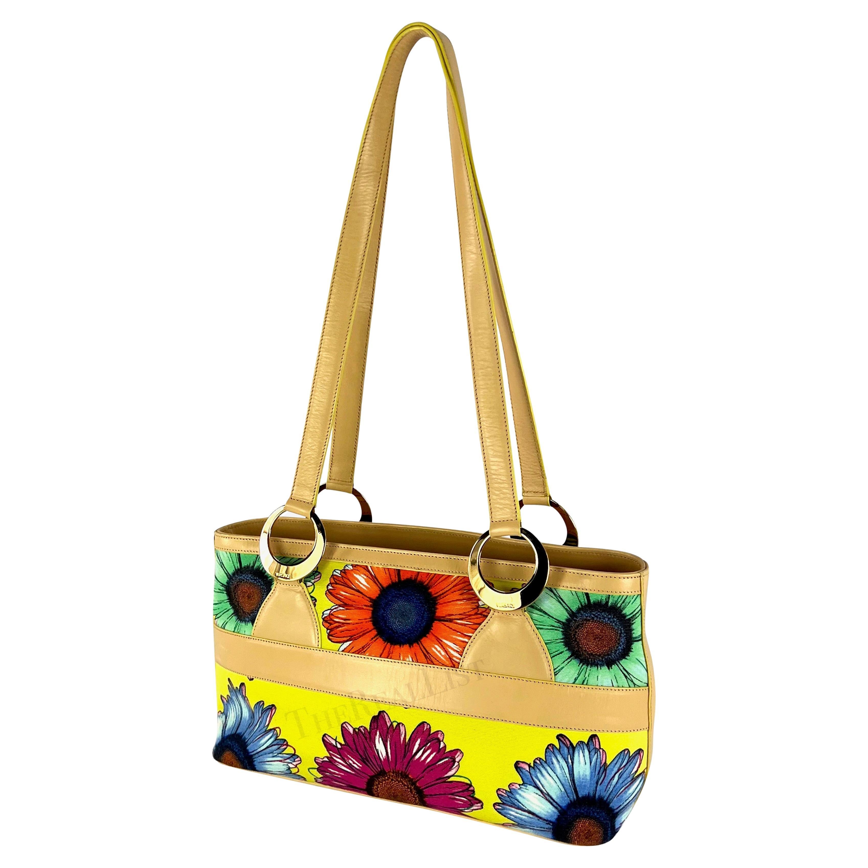 Ti presentiamo una favolosa tote a tracolla di Gianni Versace in tela floreale gialla, disegnata da Donatella Versace. Dalla collezione primavera/estate 2002, la stampa floreale evidenziata su questa borsa ha debuttato sulla passerella della