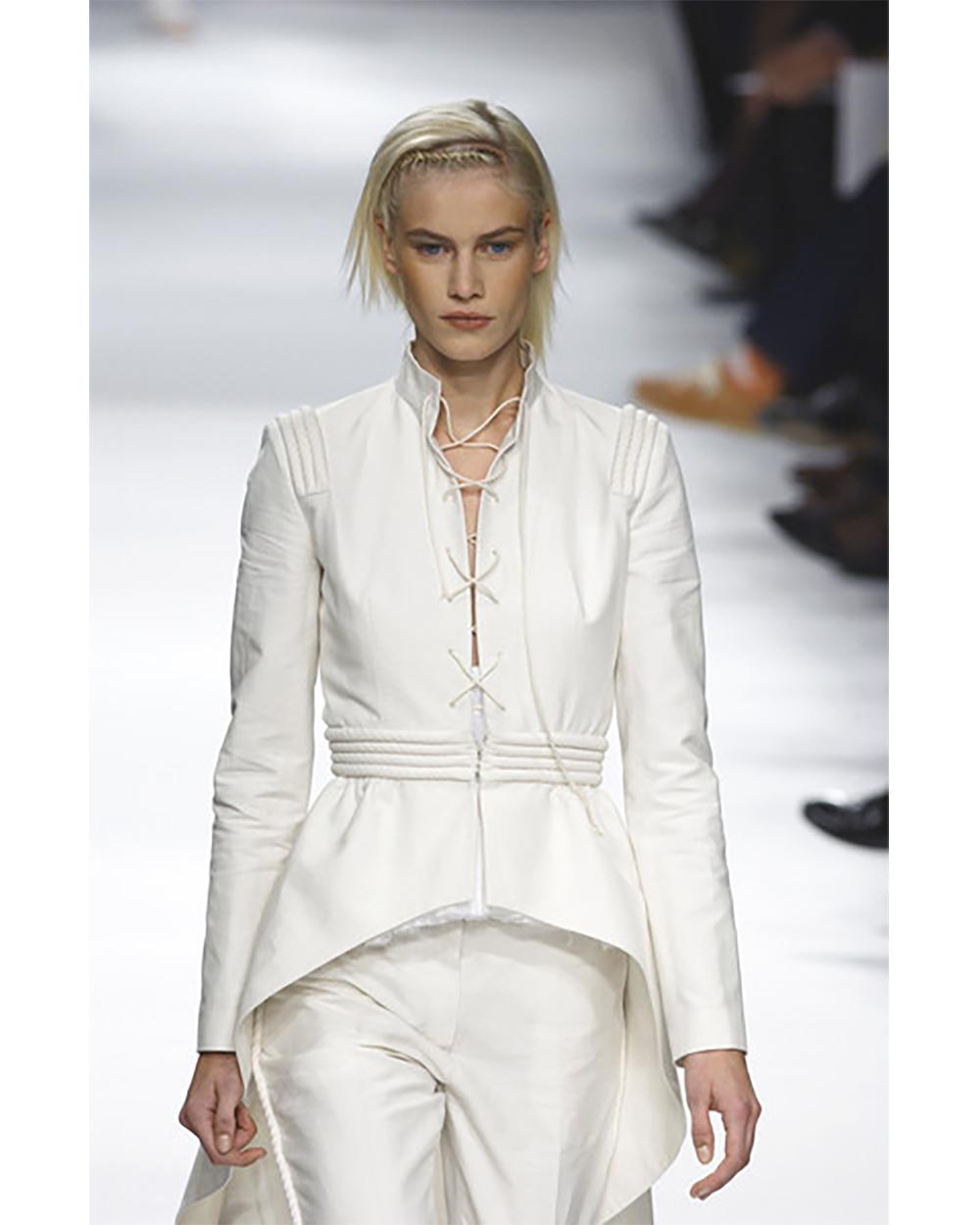 S/S 2002 Givenchy cream cotton suit set with high-low jacket and slim fit pants. Cadet-style coat with long tails, stand collar, rope shoulder and waist detailing. Lace front closure. Pants trimmed with covered rope, with front fly closure. As seen