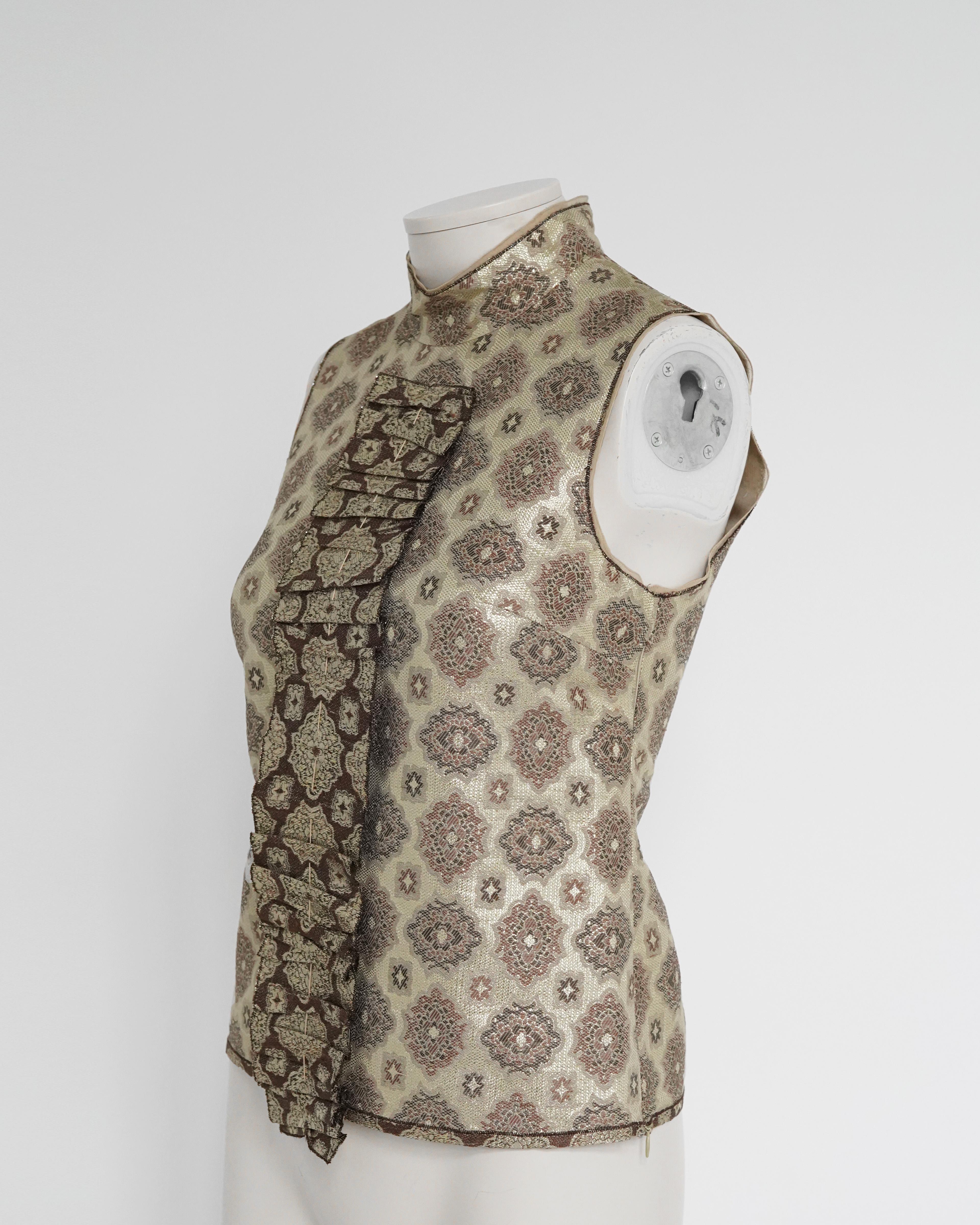 Voici une blouse sans manches en lamé doré à motifs décoratifs de Prada S/S 2002, ornée d'un large panneau à volants. La collection S/S 2002 était axée sur une nouvelle perspective du lamé - déconstruit et restructuré pour créer une image somptueuse