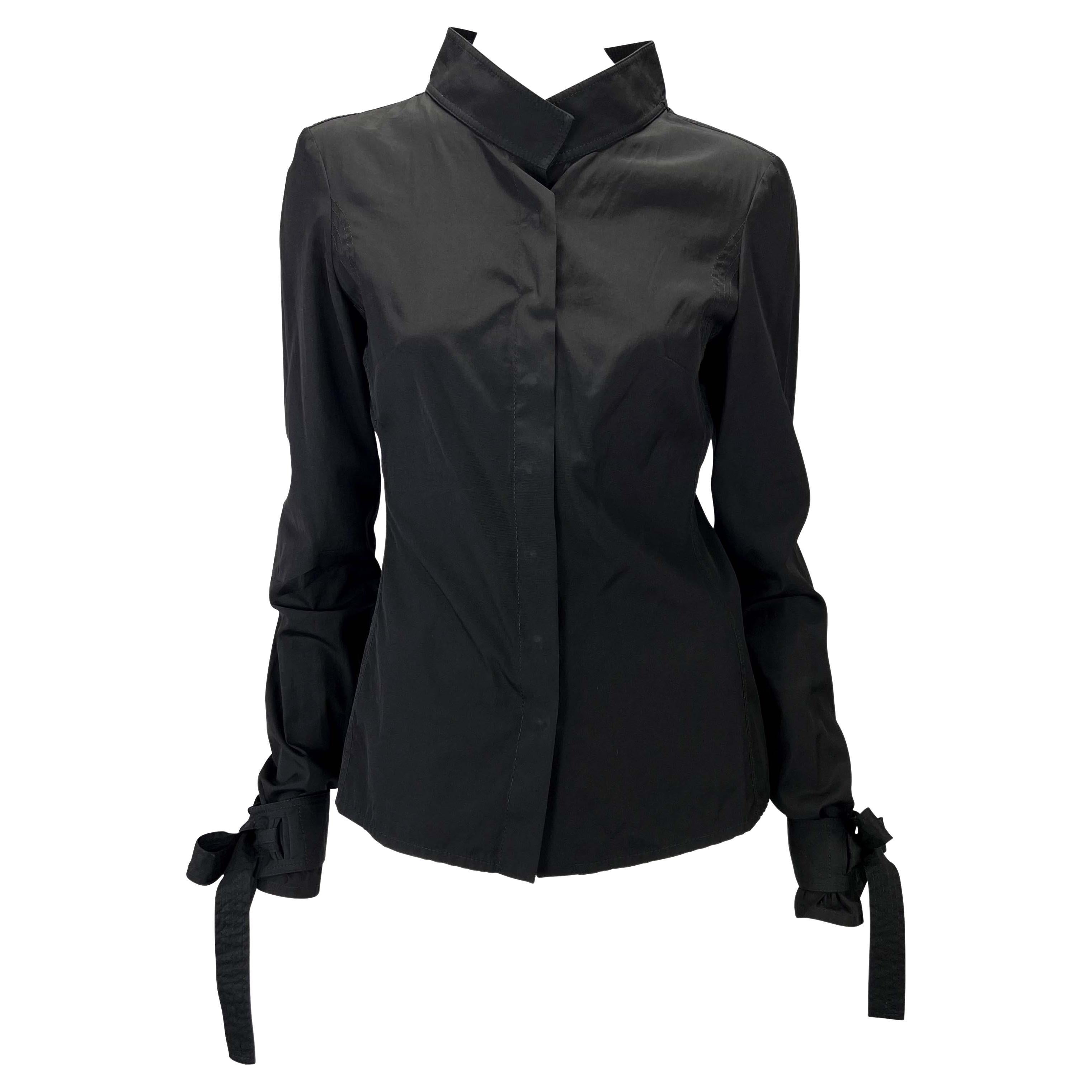 Presenting a black long sleeve Gucci shirt, designed by Tom Ford. From the Fall/Winter 2003 collection, this top features a stand-up collar, quilting near the underarm, and ties at the cuffs. Covered snap buttons grace the front of the shirt adding