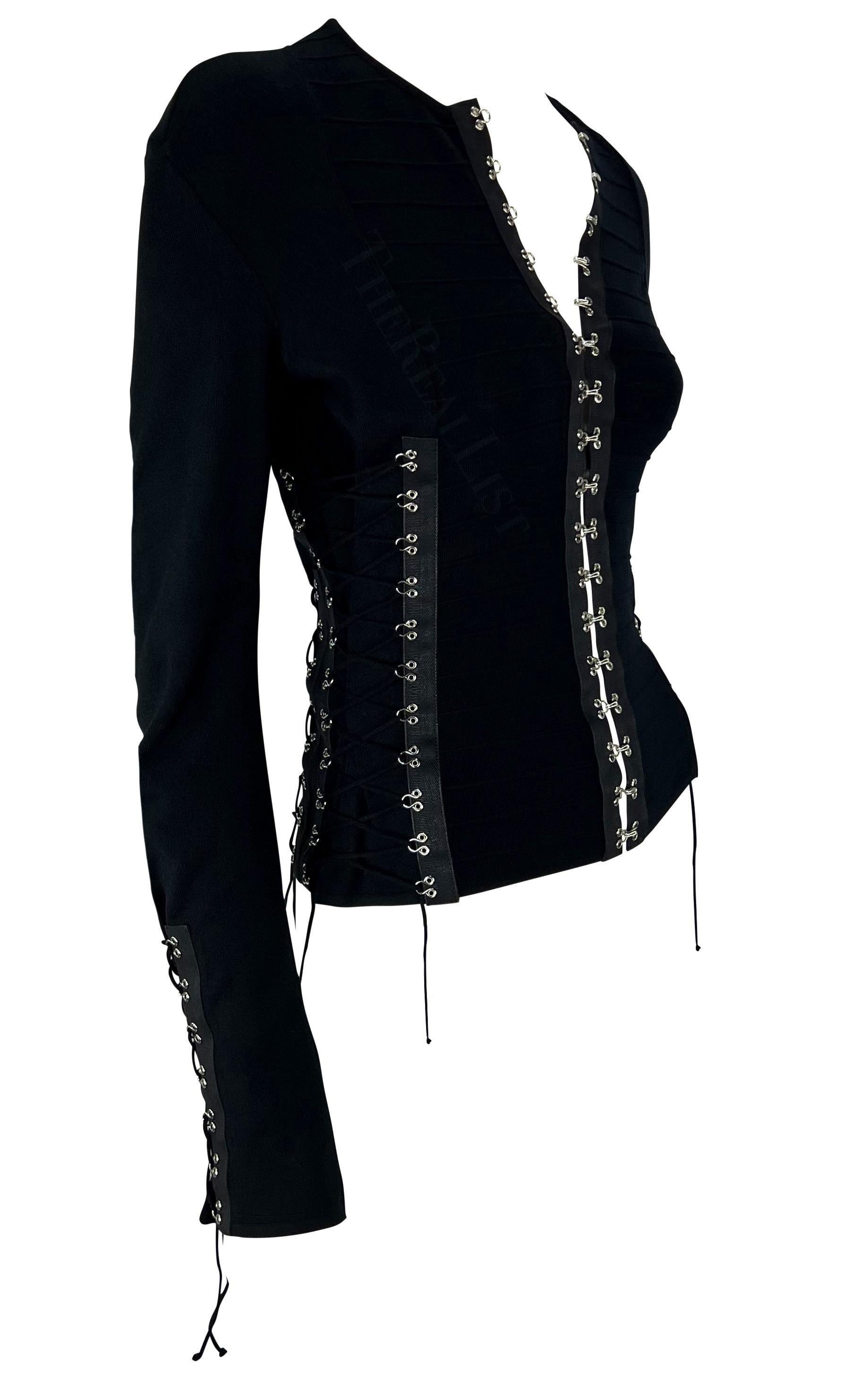 Nous vous présentons un incroyable cardigan noir en maille crochetée de John Galliano. Issu de sa collection printemps/été 2003, ce fabuleux pull à la coupe ajustée se ferme sur le devant par des crochets et des lacets autour du torse et aux