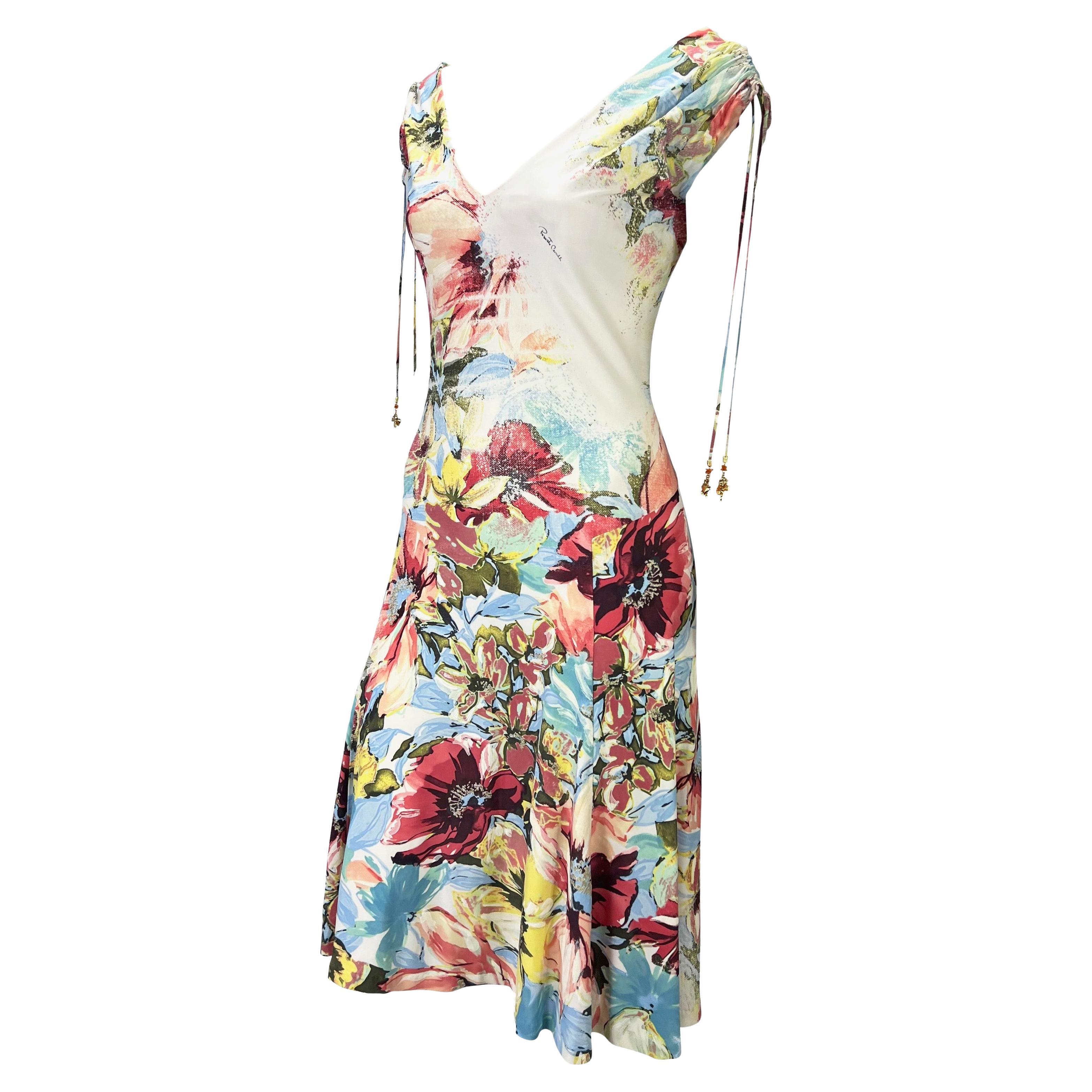 Presenting a stunning cream and multicolor floral Roberto Cavalli dress. From the Spring/Summer 2003 collection, this off-the-shoulder dress features a v-neckline, flared skirt, and hanging charms coming from the shoulder. Effortlessly chic, this