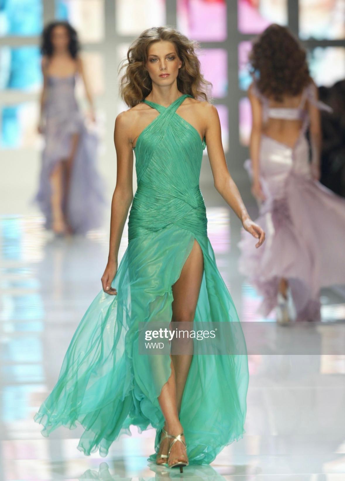 Nous vous présentons une superbe robe dos nu vert métallique Atelier Versace, créée par Donatella Versace. Issue de la collection printemps-été 2004, cette robe a fait ses débuts sur le podium du prêt-à-porter en tant que look 53, porté par Daria