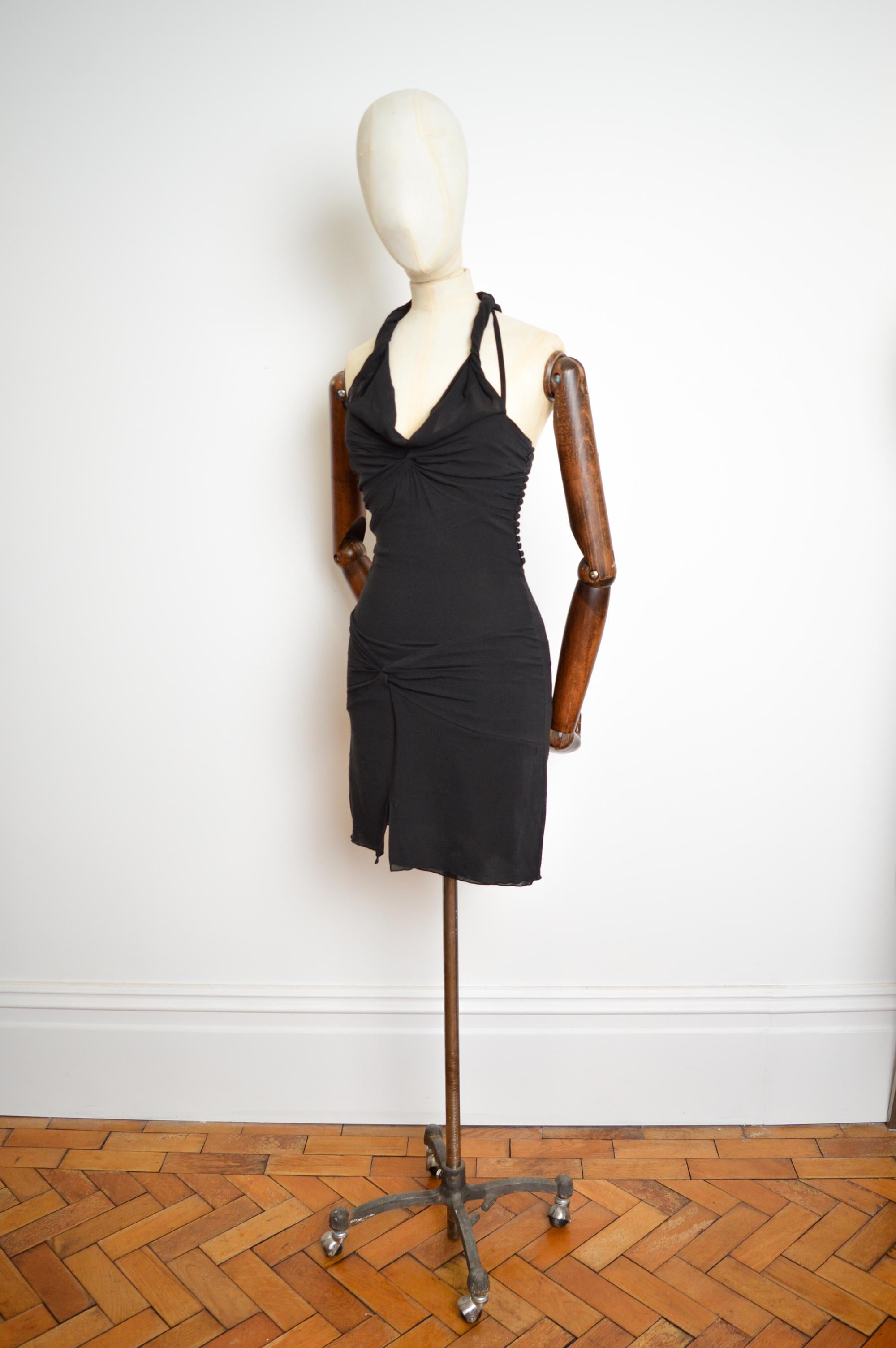 Este precioso minivestido de crepé de seda negro para la Colección Primavera/Verano 2004 de Christian Dior, diseñado por John Galliano, tiene una silueta magnífica (elástica) que se adapta a la figura, numerosos botones de tela en los detalles
