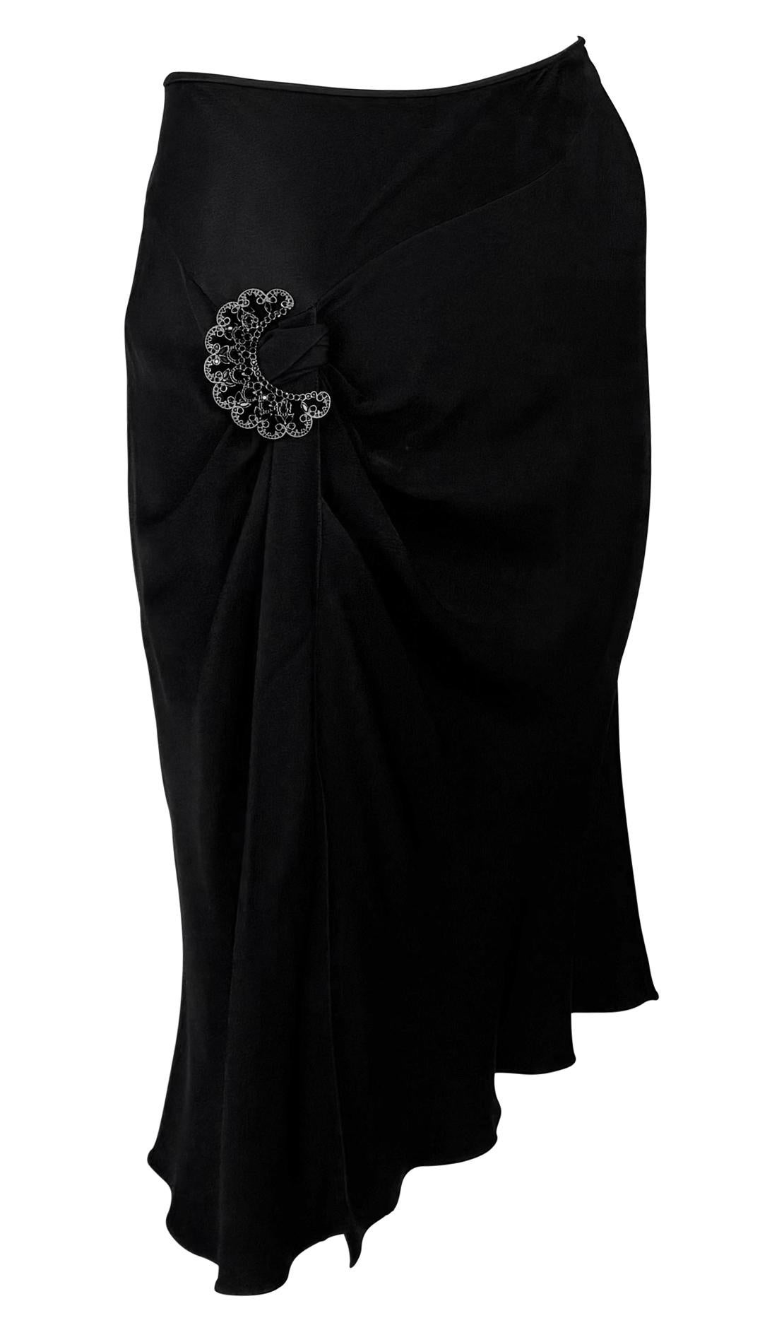 From Christian Dior’s Spring/Summer 2004 collection by John Galliano, this black satin skirt features a draped silhouette gathered at the hip with a crescent-shaped rhinestone brooch.  A series of fabric-covered buttons along one side, a Galliano