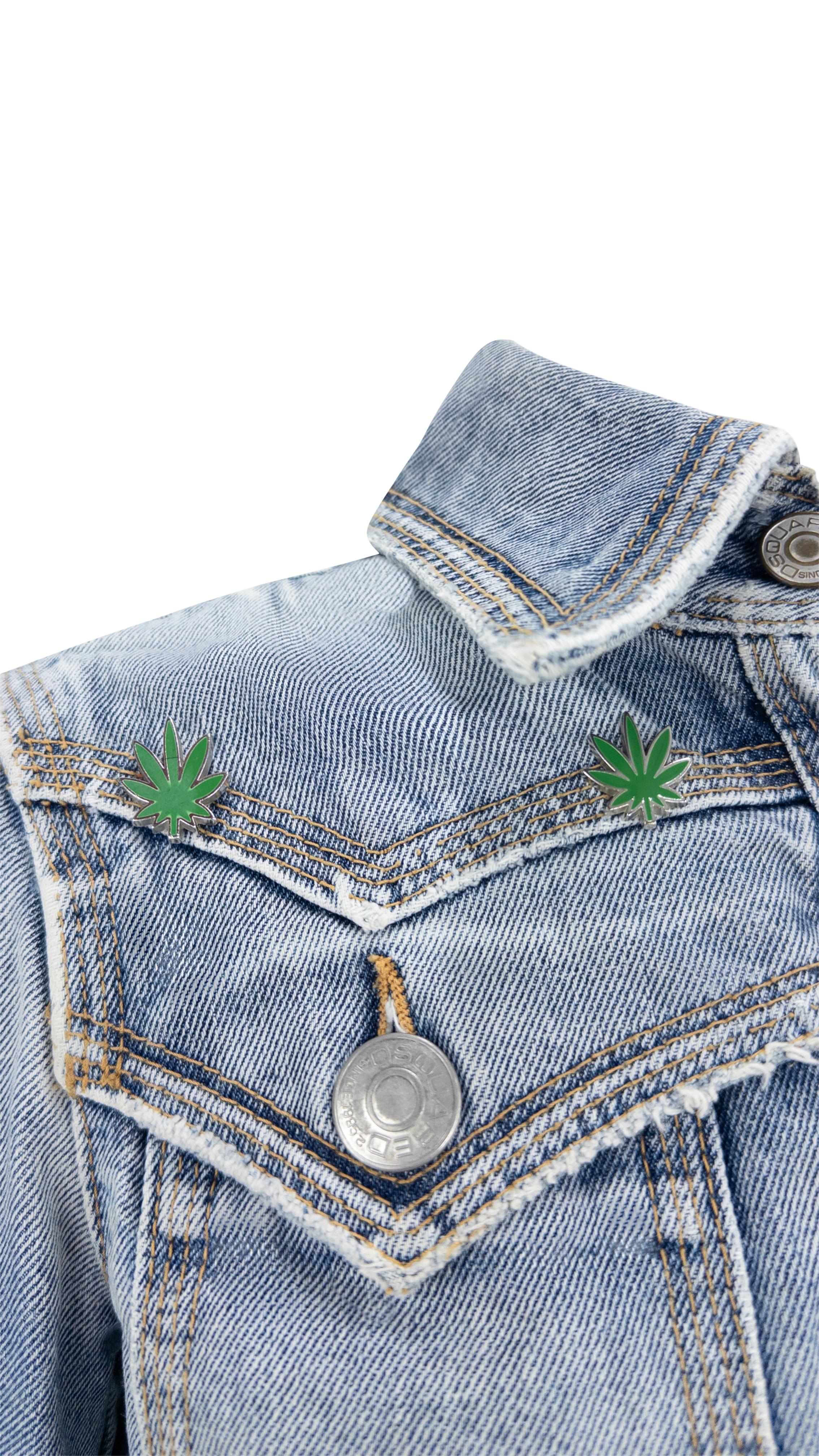 Issue de la collection printemps-été 2005 de Dsquared2, cette veste en denim délavé délavé présente une silhouette courte et des poches à rabat sur la poitrine. Les accents de feuilles de marijuana en émail vert sur les épaules ajoutent une touche