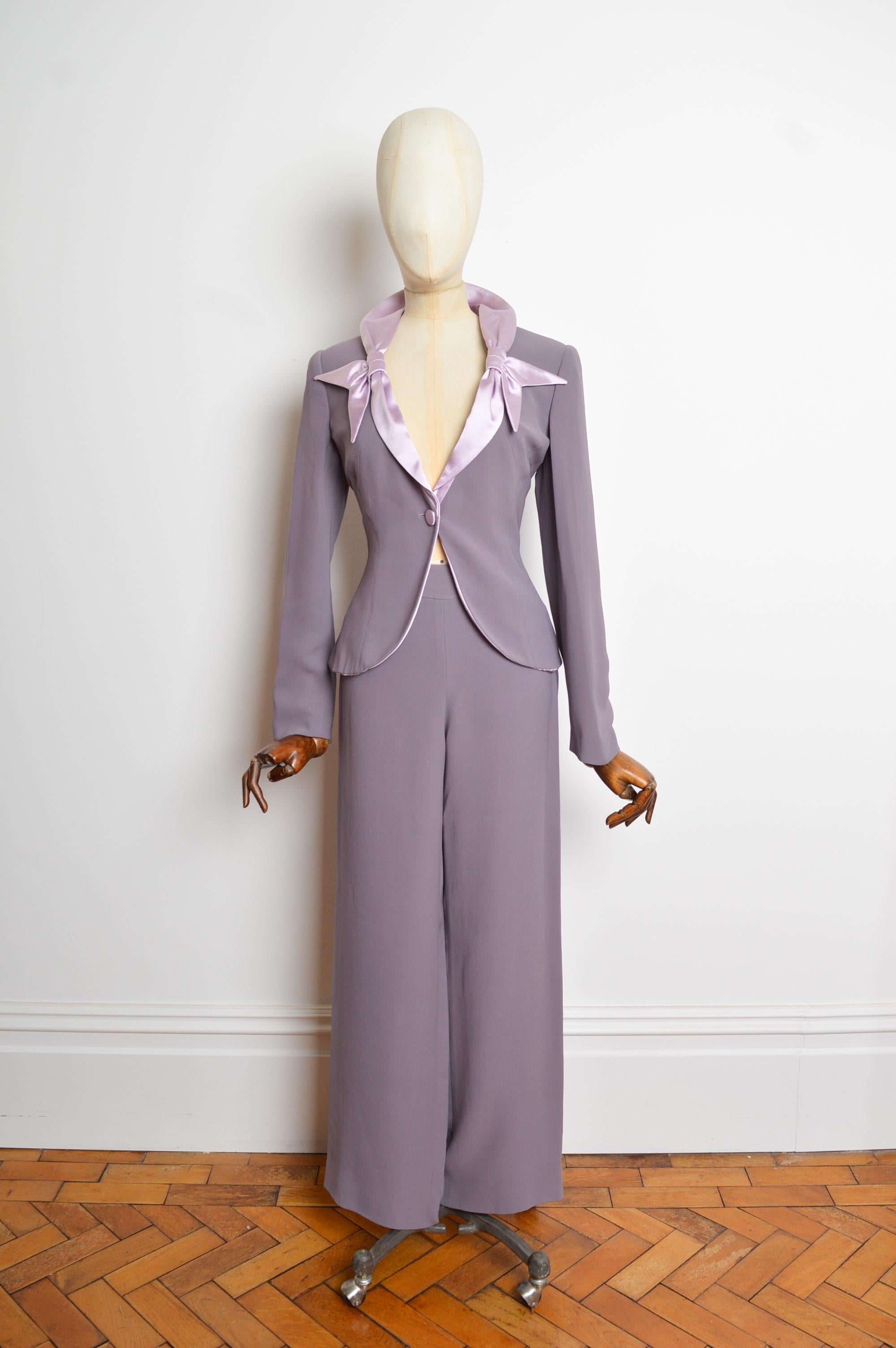 Giacca e pantaloni Blazer primavera 2005 Giorgio Armani lilla e viola.
Questo superbo ensemble è realizzato al 100% in pura seta e presenta un esterno opaco con fodera interna e revers in raso. L'abito è caratterizzato da una silhouette aderente e