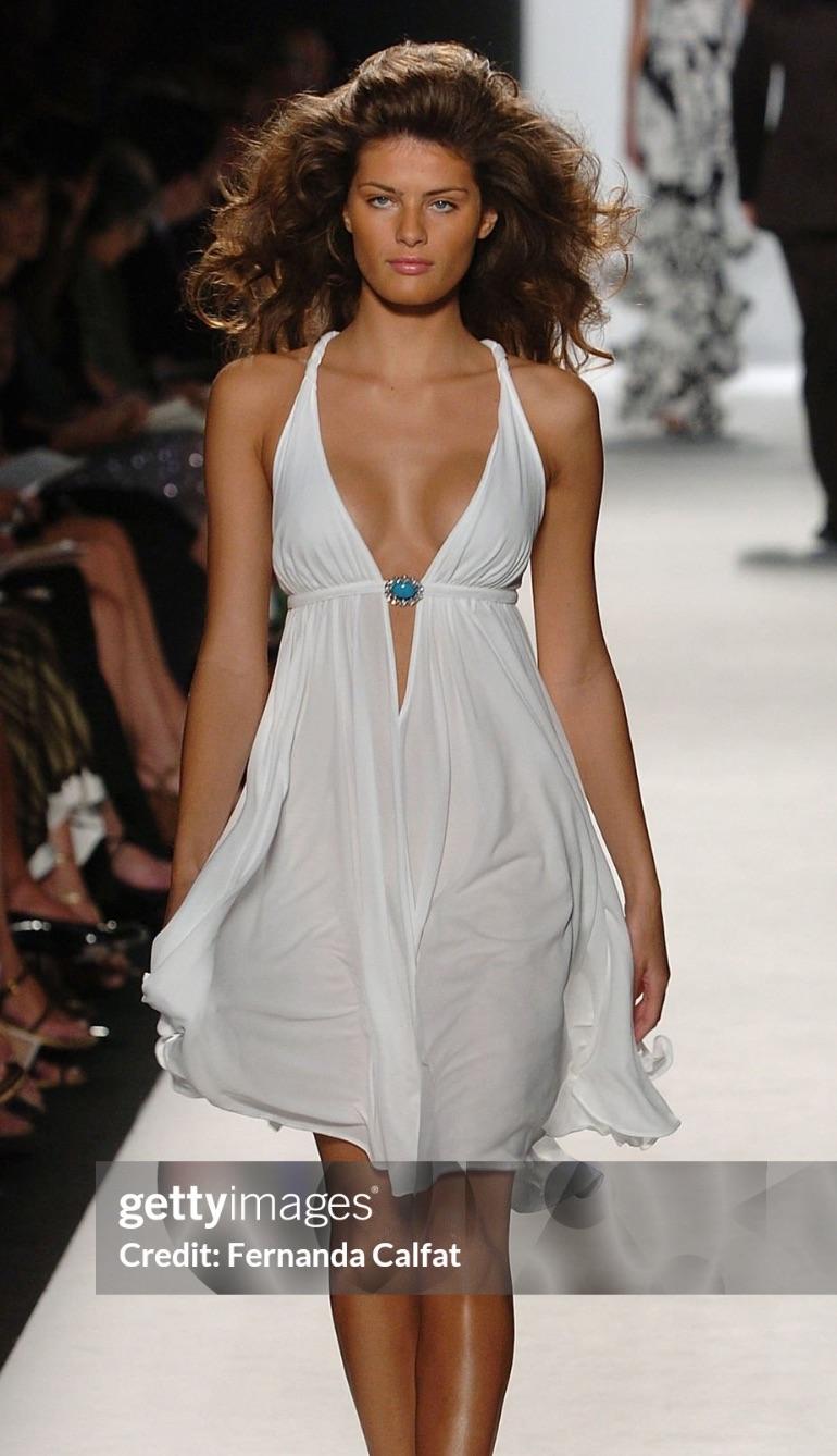 From Michael Kors’ Spring/Summer 2005 collection, this white halter mini dress features a plunging neckline gathered at the bust with a turquoise brooch detail. The flared skirt and open back with crisscross ties evoke a breezy glamour.

Approximate