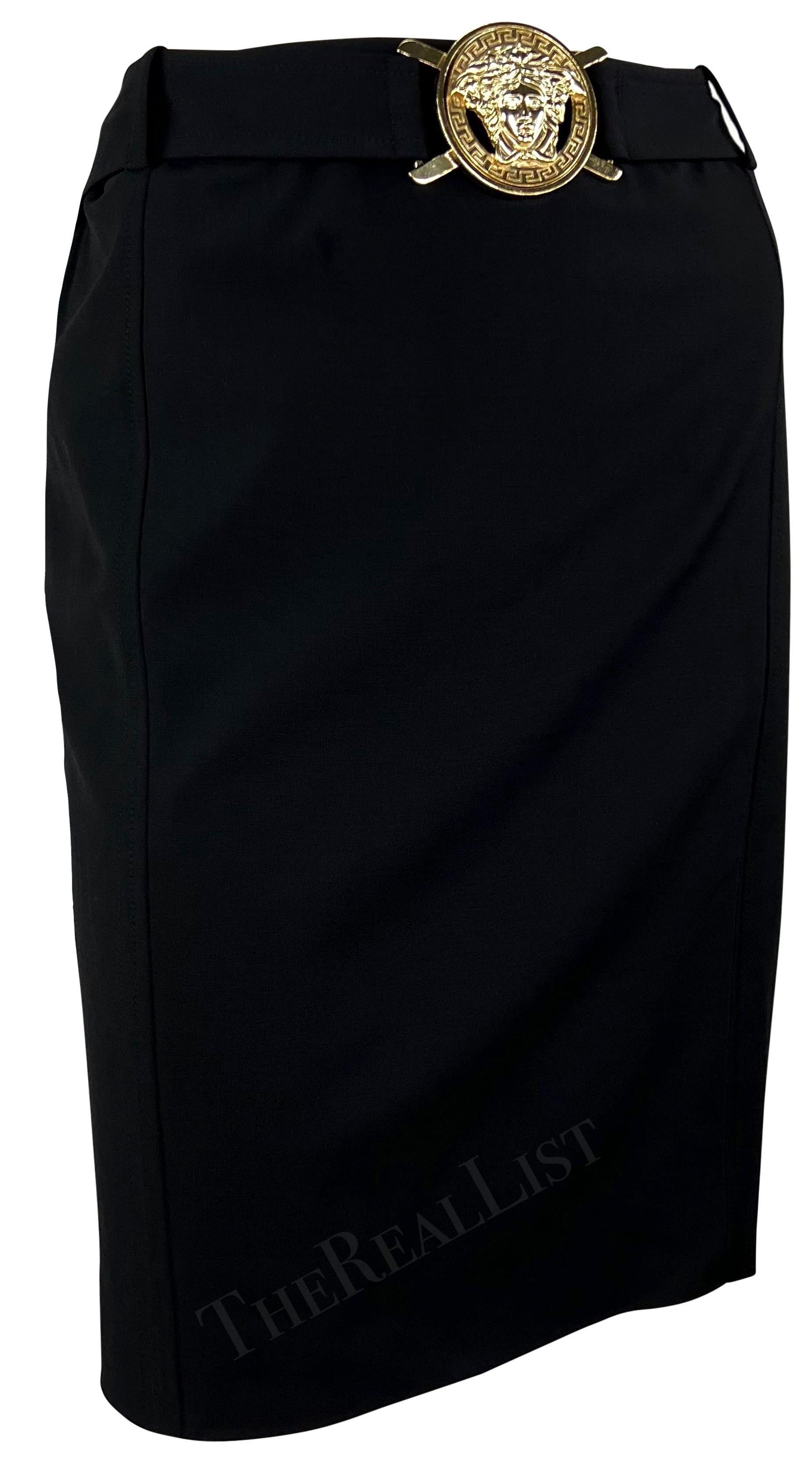 Nous vous présentons une jupe noire chic à taille haute de Versace, créée par Donatella Versace et issue de la collection printemps/été 2005. Cette jupe au genou présente une ceinture cousue à la taille, ornée d'une boucle Versace Medusa proéminente
