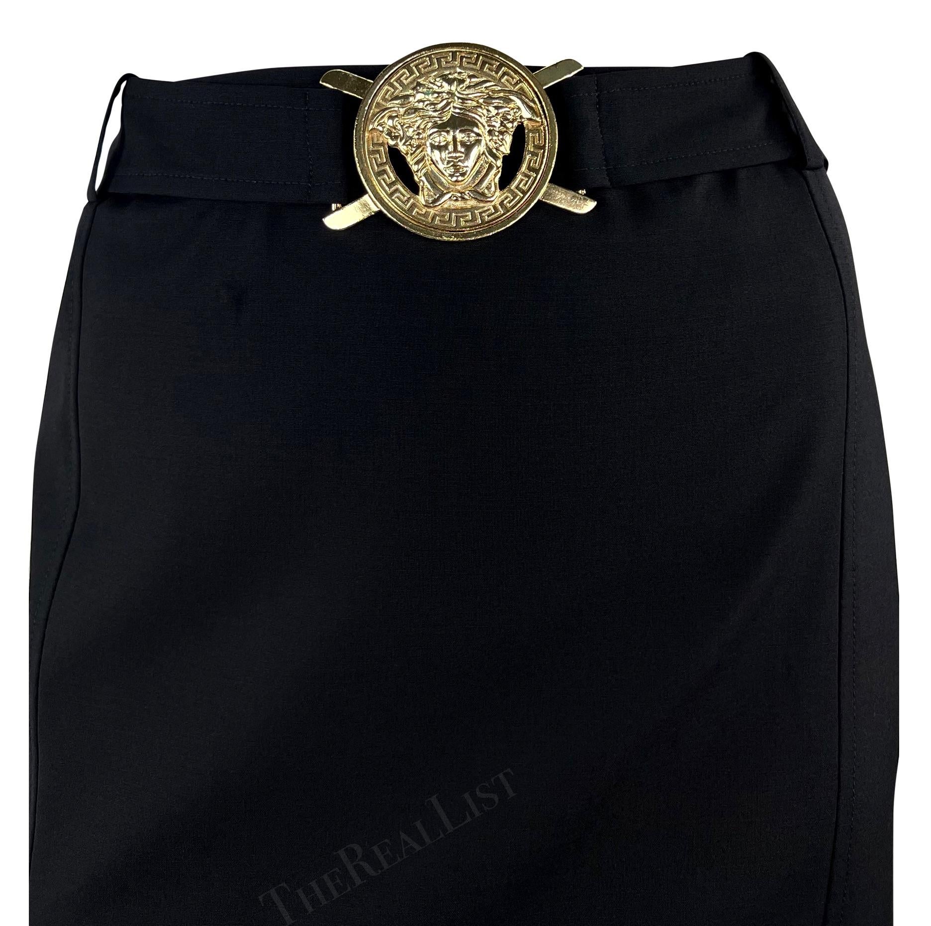 Presenting a chic black high-waisted skirt by Versace, designed by Donatella Versace from the Spring/Summer 2005 collection. This knee-length skirt showcases a sewn-in waist belt adorned with a prominent Versace Medusa buckle at the