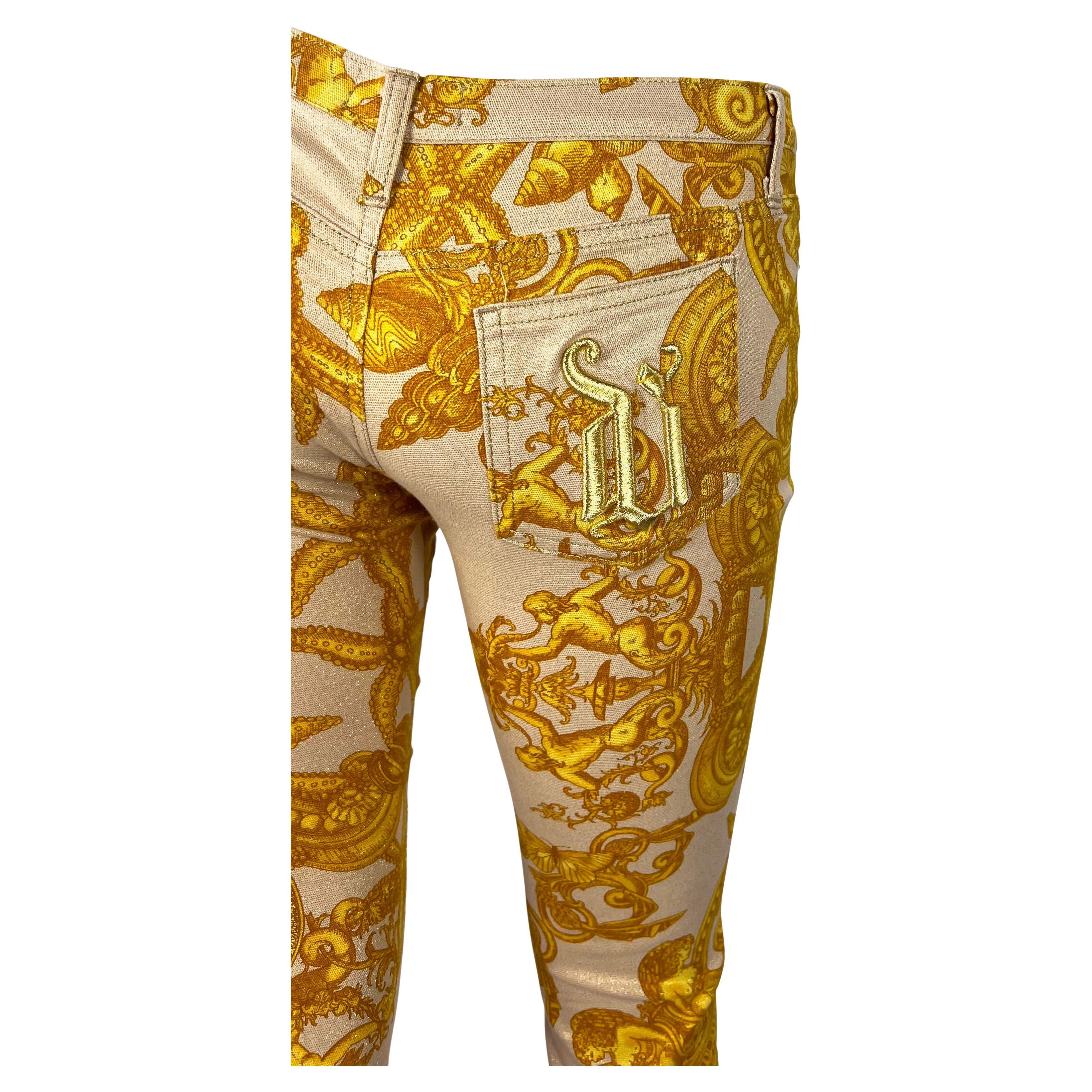 Presenting a pair of low-rise pink and gold Versace jeans, designed by Donatella Versace. From the Spring/Summer 2005 collection, these pants feature a lively gold marine-themed baroque print atop a light pink background. The jeans are made complete