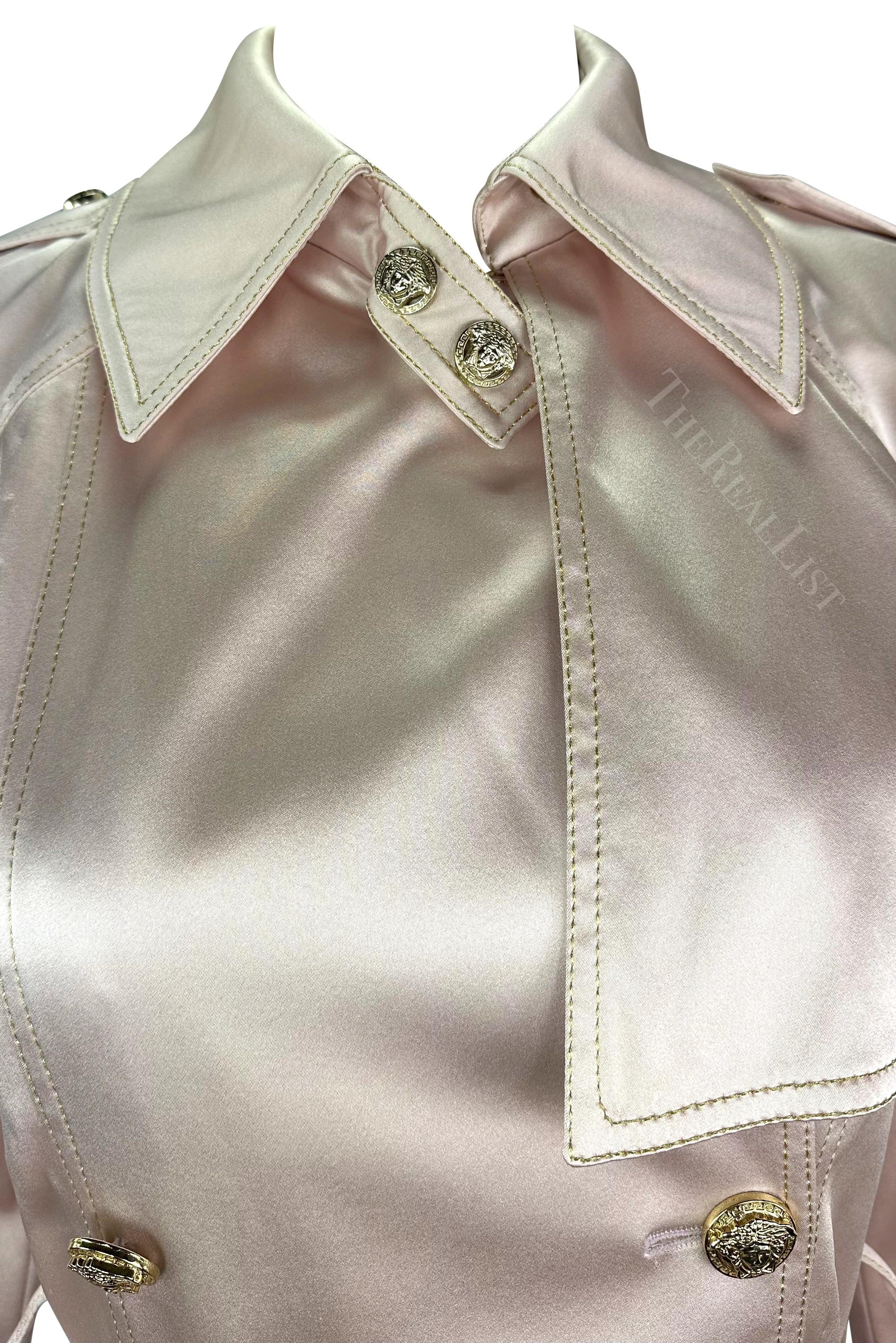 Presentamos un abrigo prototipo Versace atemporal de satén rosa claro con doble botonadura, diseñado por la legendaria Donatella Versace. De la colección Primavera/Verano 2005, este abrigo excepcional desprende una lustrosa construcción de satén