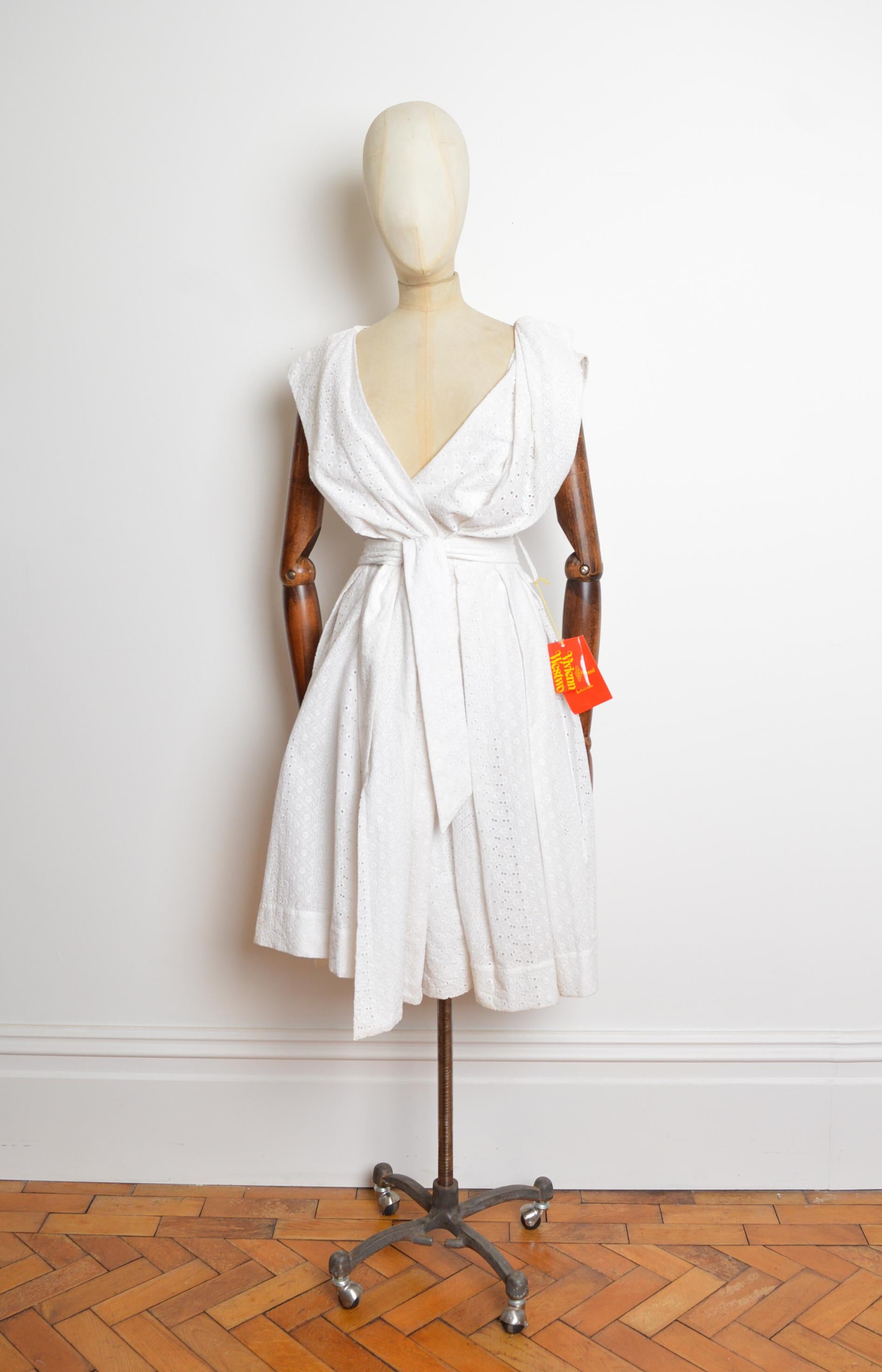 Ein schönes S/S 2007 Vivienne Westwood Broderie anglaise Teekleid.
Das Kleid ist aus weißer Baumwolle gefertigt, hat einen tiefen V-Ausschnitt, eine taillierte Passform mit verstellbarem Taillengürtel mit Bindeband, einen Knopfverschluss und einen