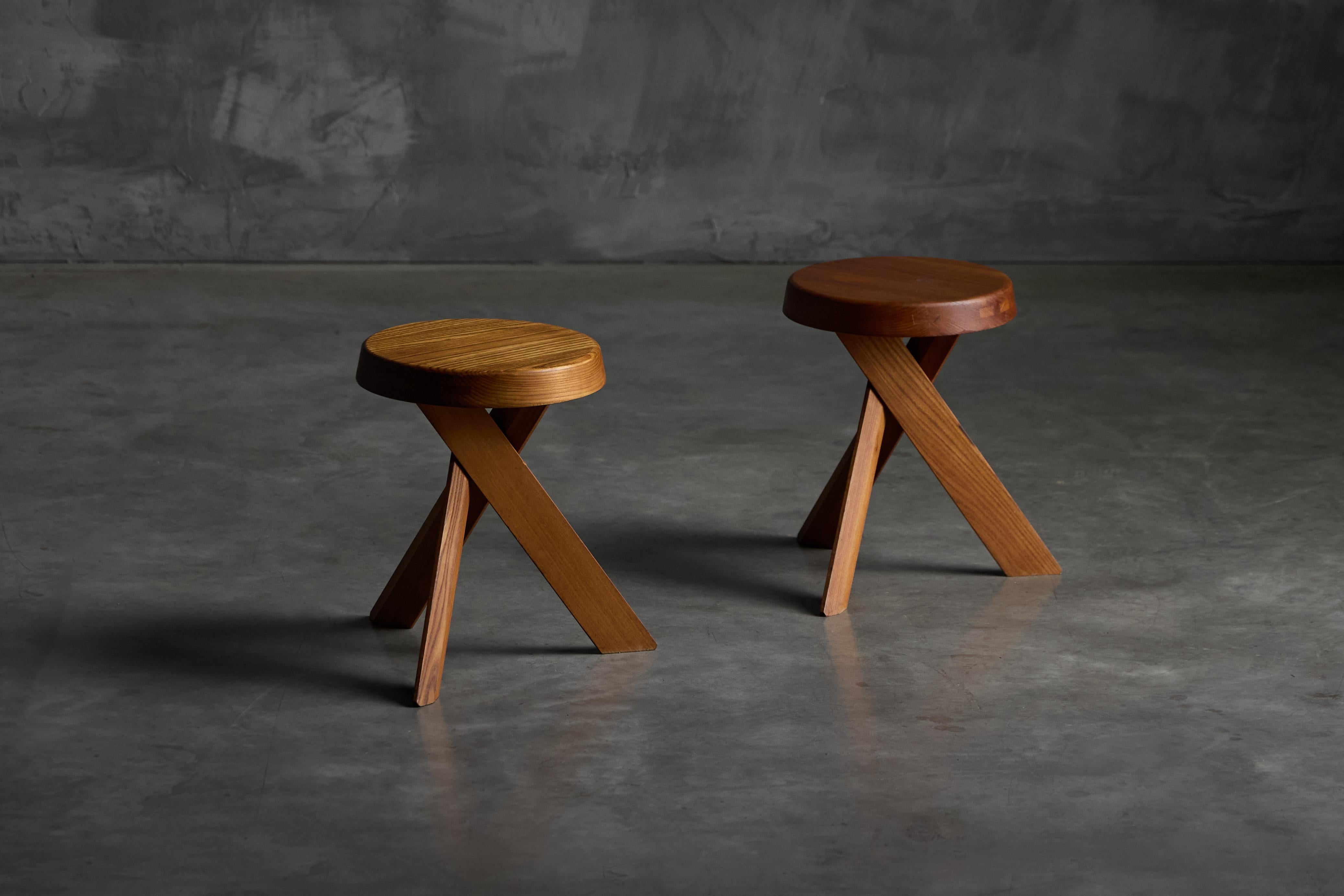 Les tabourets Early edition de Pierre Chapo, méticuleusement fabriqués en bois d'orme massif dans la France des années 1970, présentent une assise épaisse avec un veinage naturel et trois pieds croisés. Les joints visibles le long du bord de