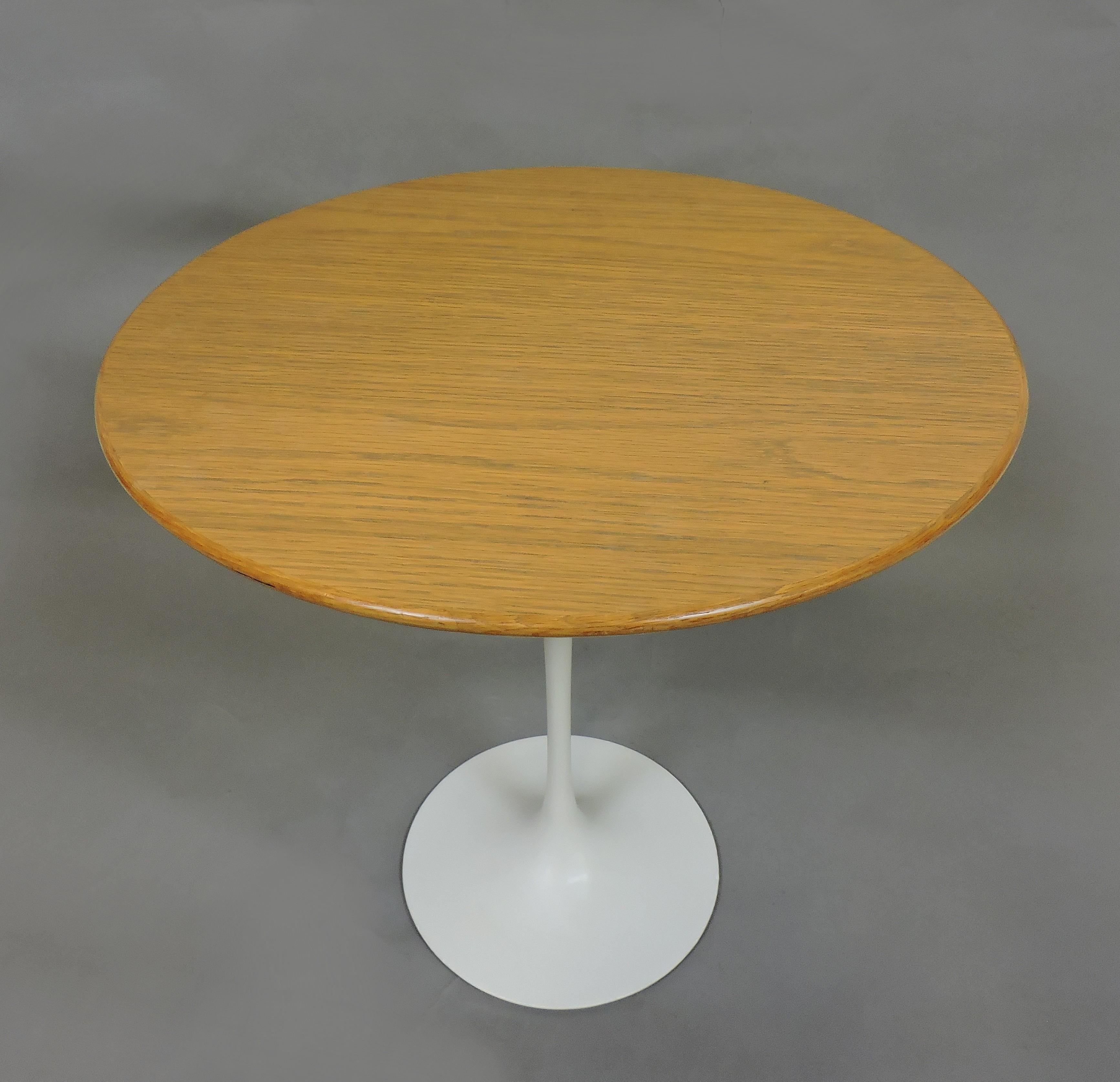Classic tulip side table designed by Eero Saarinen and manufactured by Knoll. This table has a 20 inch diameter oak top, a white pedestal base, and was made in 1978. Knoll label underneath.