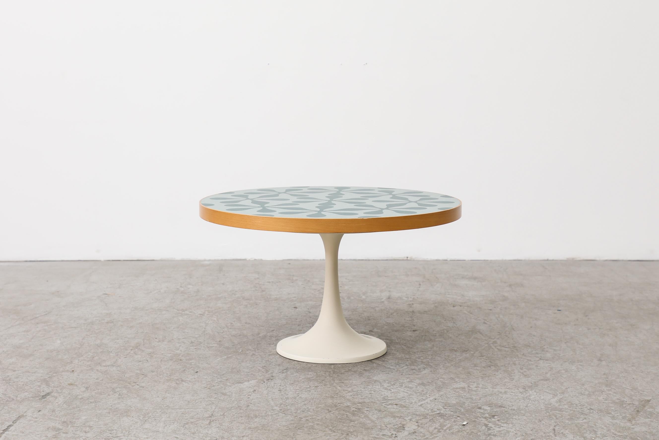 Retro table with teal flower print laminate table top, light wood edging and white enameled tulip base. A coffee or table or side table in original condition with normal wear for its age and use.