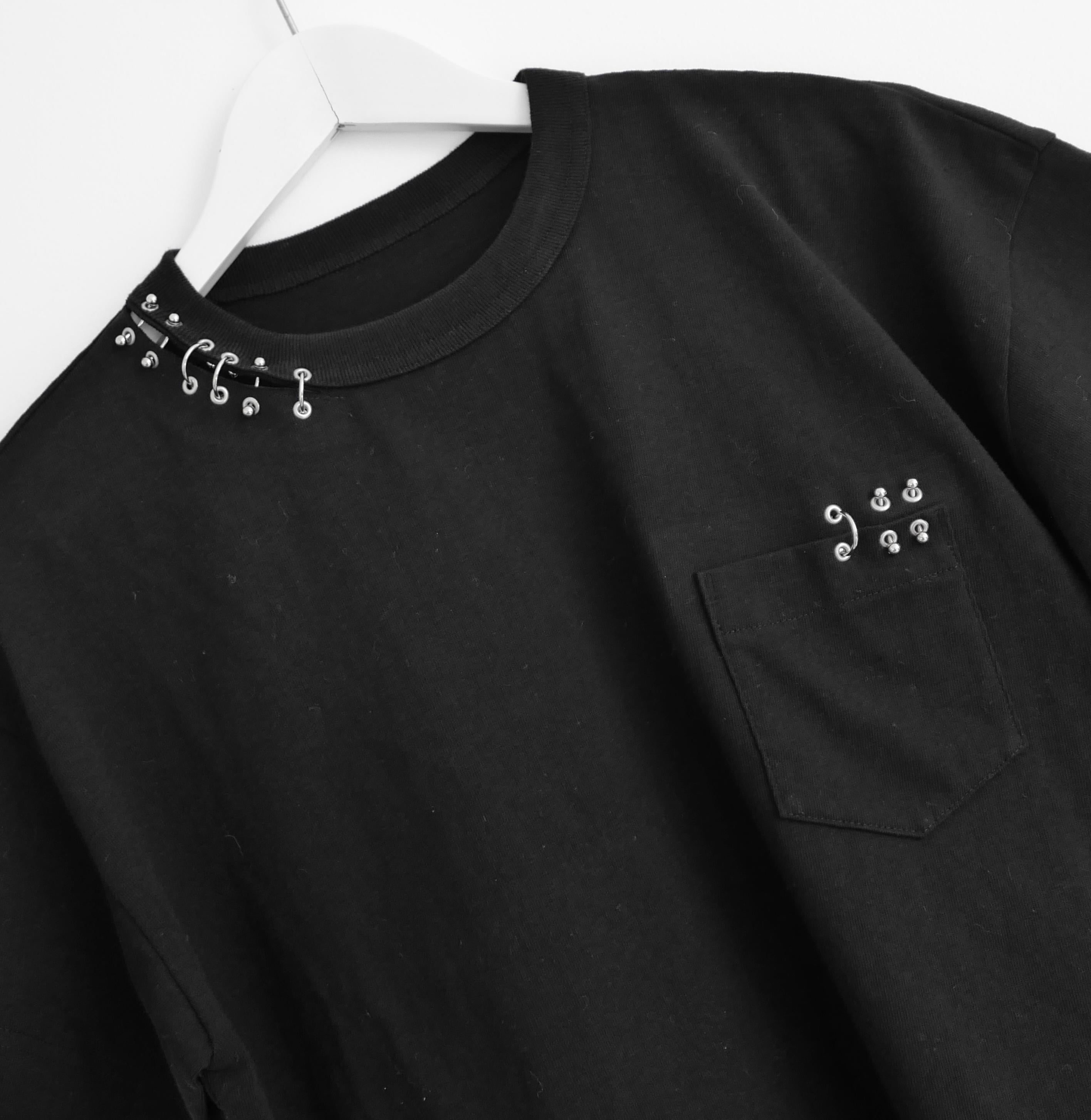 Rarissima t-shirt Sacai Piercing - nuova con etichette. Realizzata in spesso cotone nero con borchie punk in metallo e girocollo con spacco. Ha un taglio squadrato e una piccola tasca frontale. Taglia 3 con taglio oversize. Misure circa: busto 44