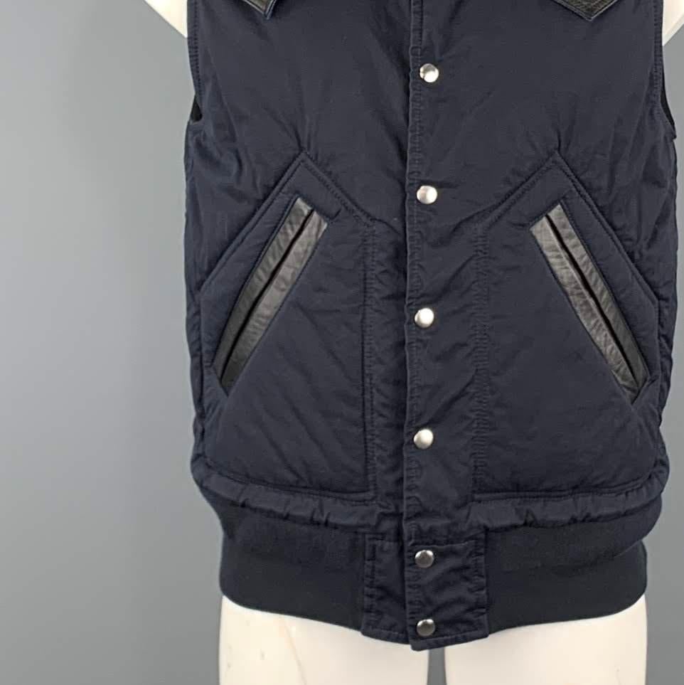 SACAI vest comes in a navy cotton blend featuring black leather trim details, buttoned closure, and front slit pockets. Made in Japan.
 
Excellent Pre-Owned Condition.
Marked: 1
 
Measurements:
 
Shoulder: 17.5 in.
Chest: 46 in.
Length: 27 in.