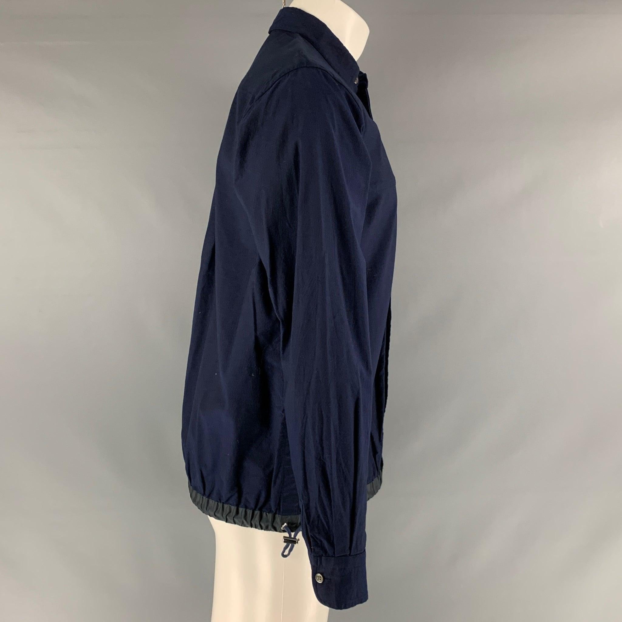 SACAI long sleeve shirt comes in a navy cotton oxford material featuring patch and welt pockets, button closure, drawstring at hem, and a button down collar. Made in Japan.Very Good Pre-Owned Condition. Minor mark at left sleeve. 

Marked:  
041
