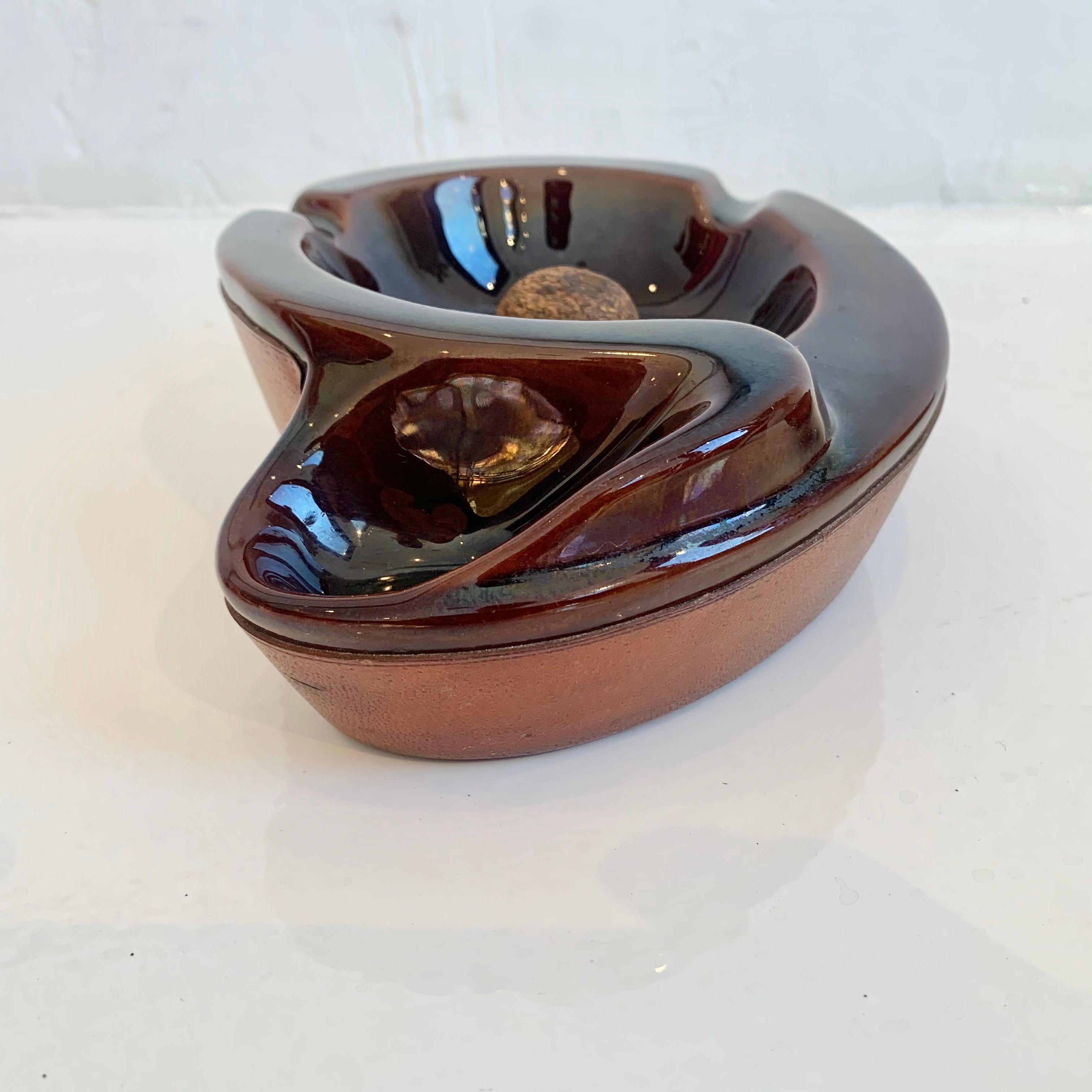 Handsome leather and ceramic ashtray/catchall by Longchamp. Biomorphic shape with inset ceramic tray and extended cigarette or pipe holder. Great saddle color leather. Great vintage condition.