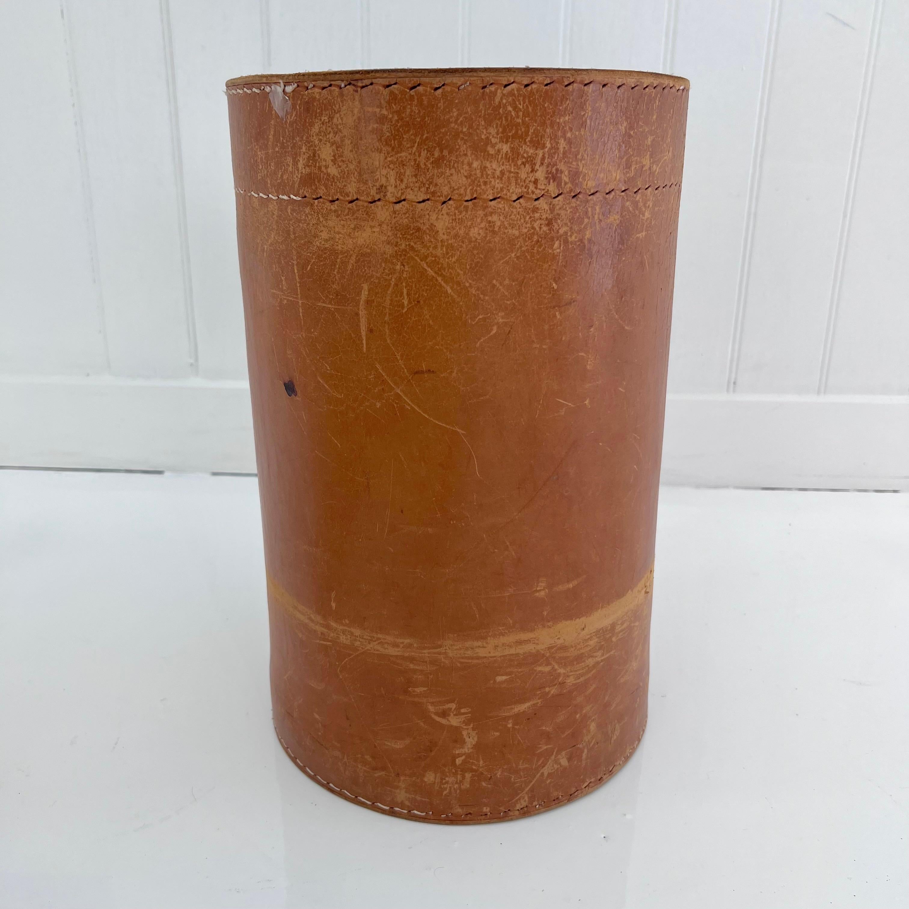 Incredible 1960s waste bin with a unique design involving a thick cowhide leather wrapped and sewn. Contrast stitching on every seam give this piece a slight Adnet style thus elevating it's appearance. Beautiful scuffs and water marks give this