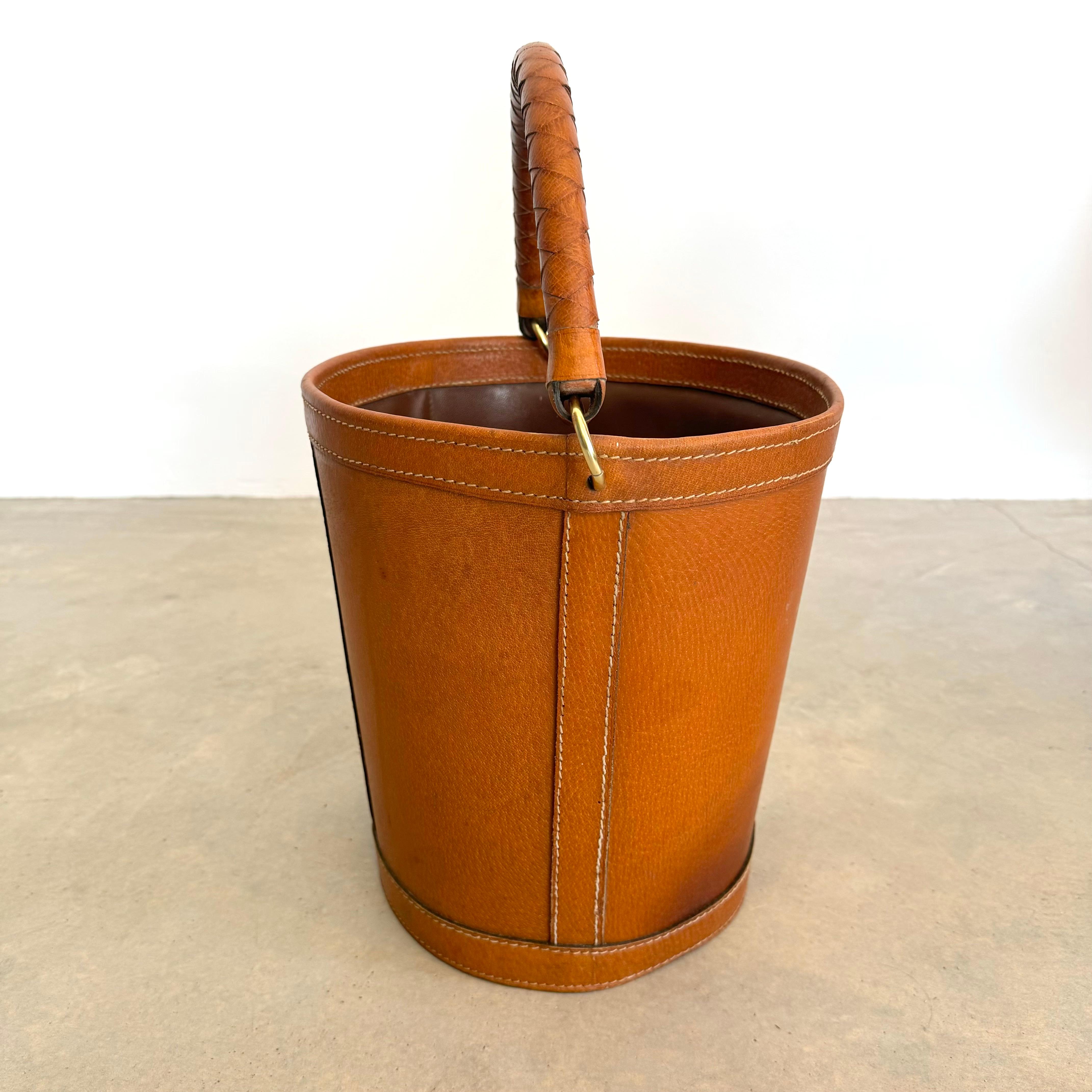 French saddle leather waste bin with a substantial braided leather handle. Great coloring to saddle leather. Large brass ring hardware. Contrast stitch throughout. plastic lining inside the bin to protect the leather against soiling or staining.