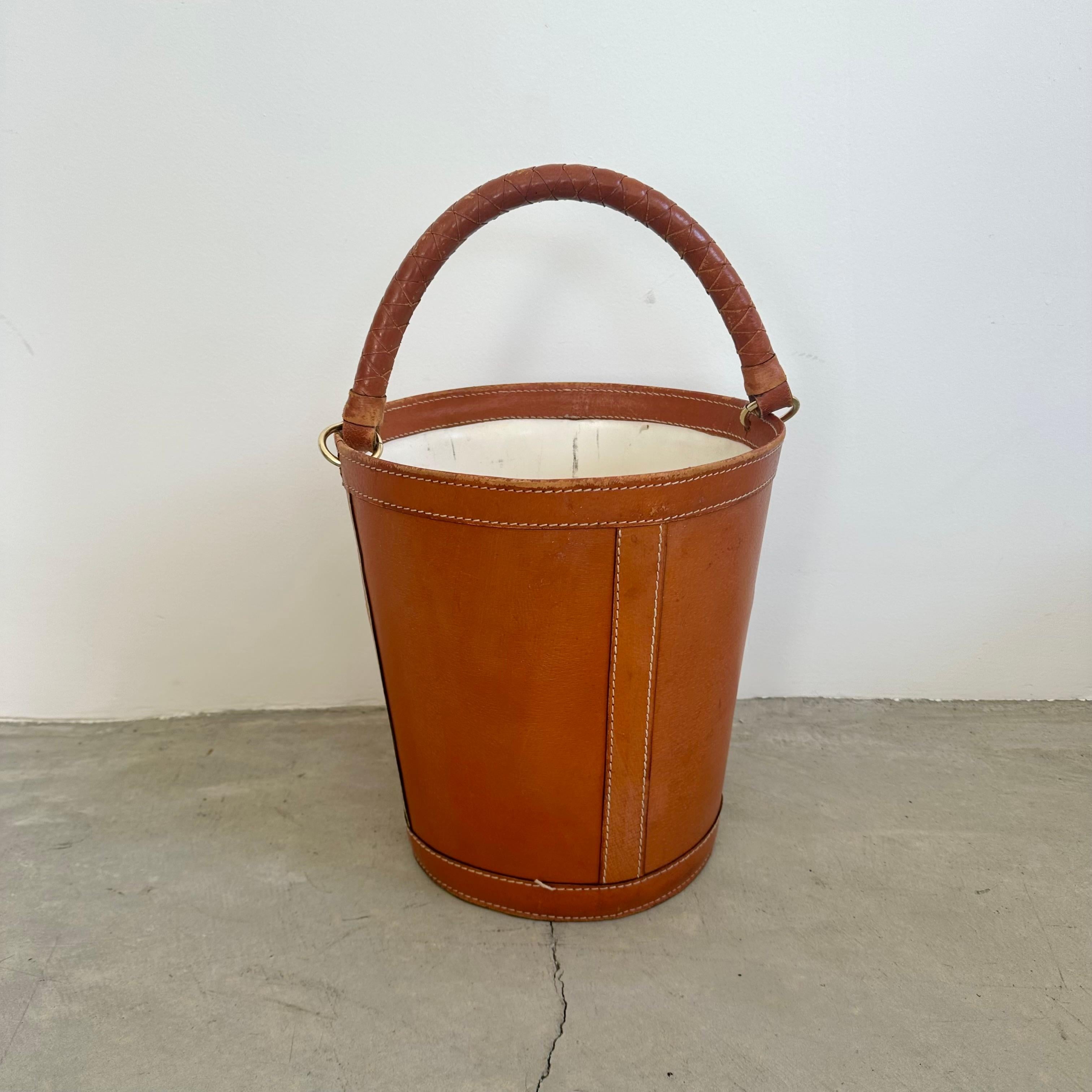 Poubelle en cuir de selle français avec une importante poignée en cuir tressé. Une belle coloration pour le cuir de la selle. Grand anneau de quincaillerie en laiton. Coutures contrastées sur l'ensemble du corps. Doublure en plastique à l'intérieur