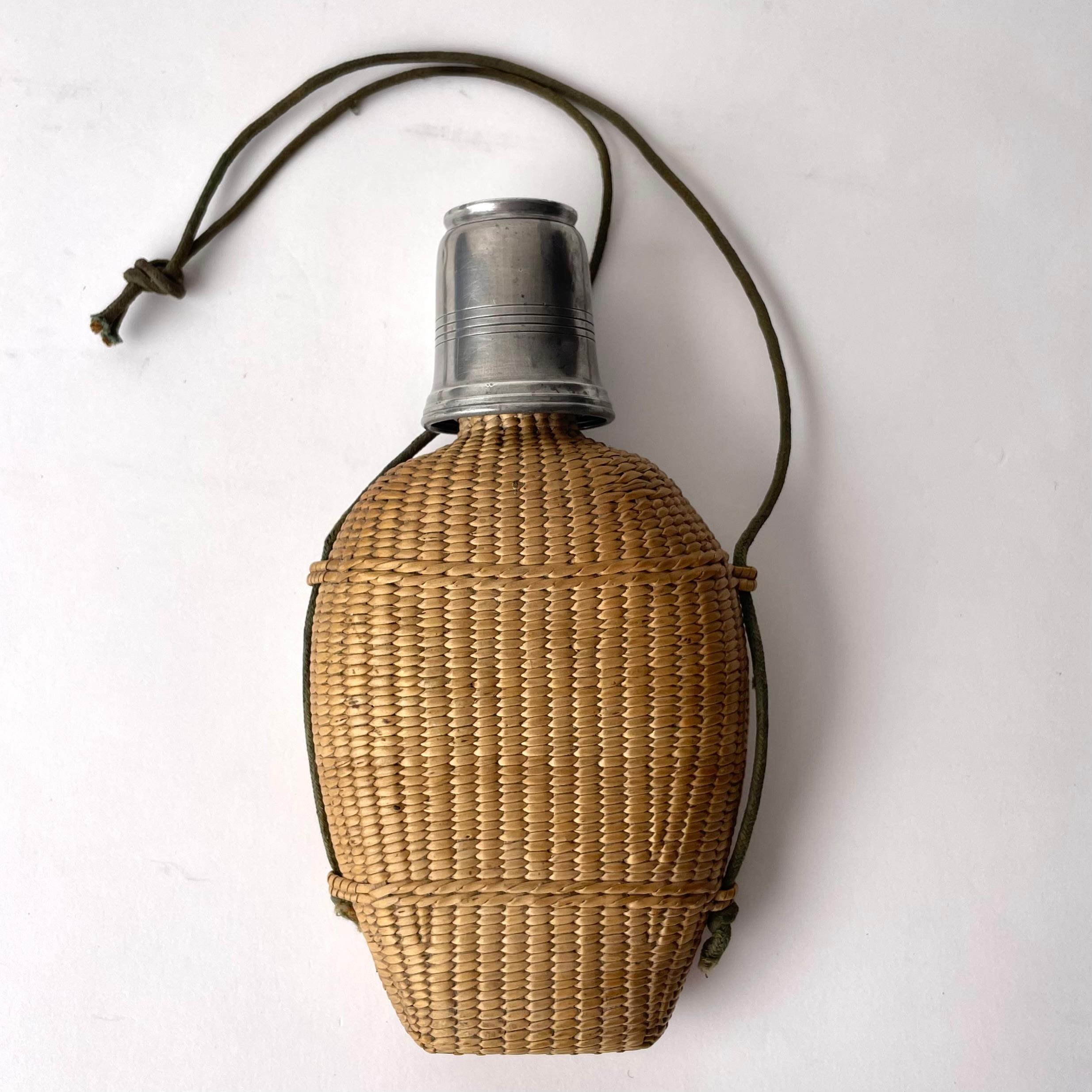 Safari Canteen Bottle, Rattan, Glass and Tin, probably late 19th C/early 20th C

A charming canteen bottle or flask, inspired by the fashion and style of safari and tropical exploration. The bottle is encased in a beautiful rattan covering, and
