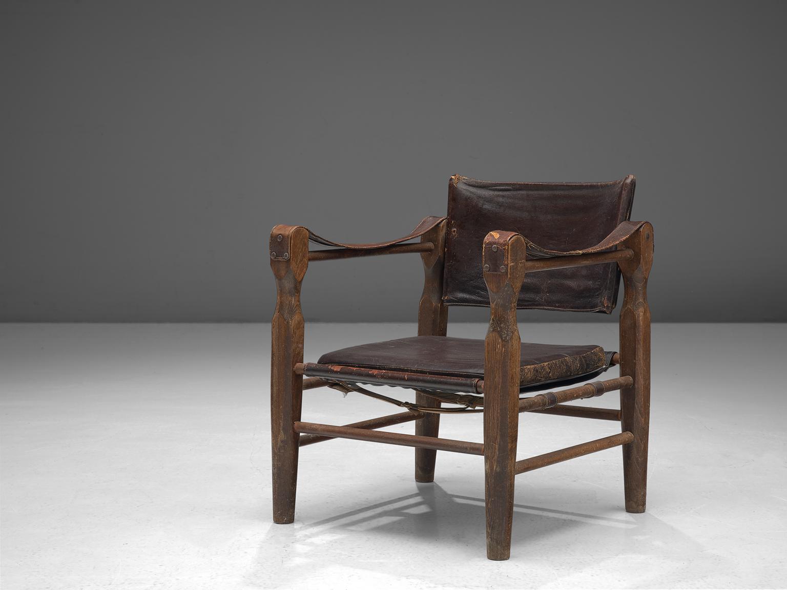 Safari chair, oak and leather, Europe, 1940s.

Robust yet stately safari chair that gained a very rich patina. This armchair features wonderfully carved wooden legs that raise up and hold up the leather straps that function as armrests. These